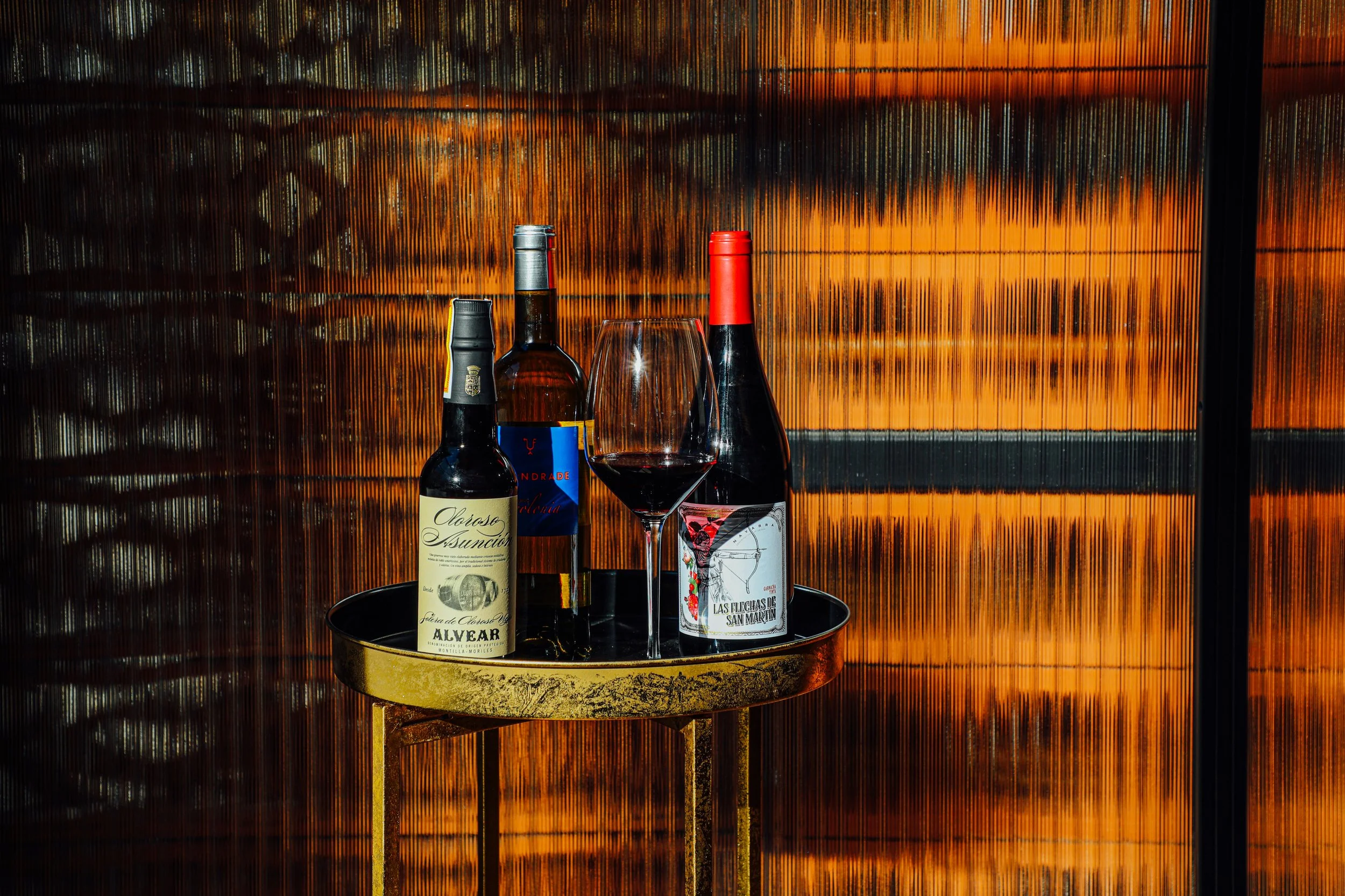 Five bottles of wine and a wine glass on a small round table, set against a textured orange and black background.