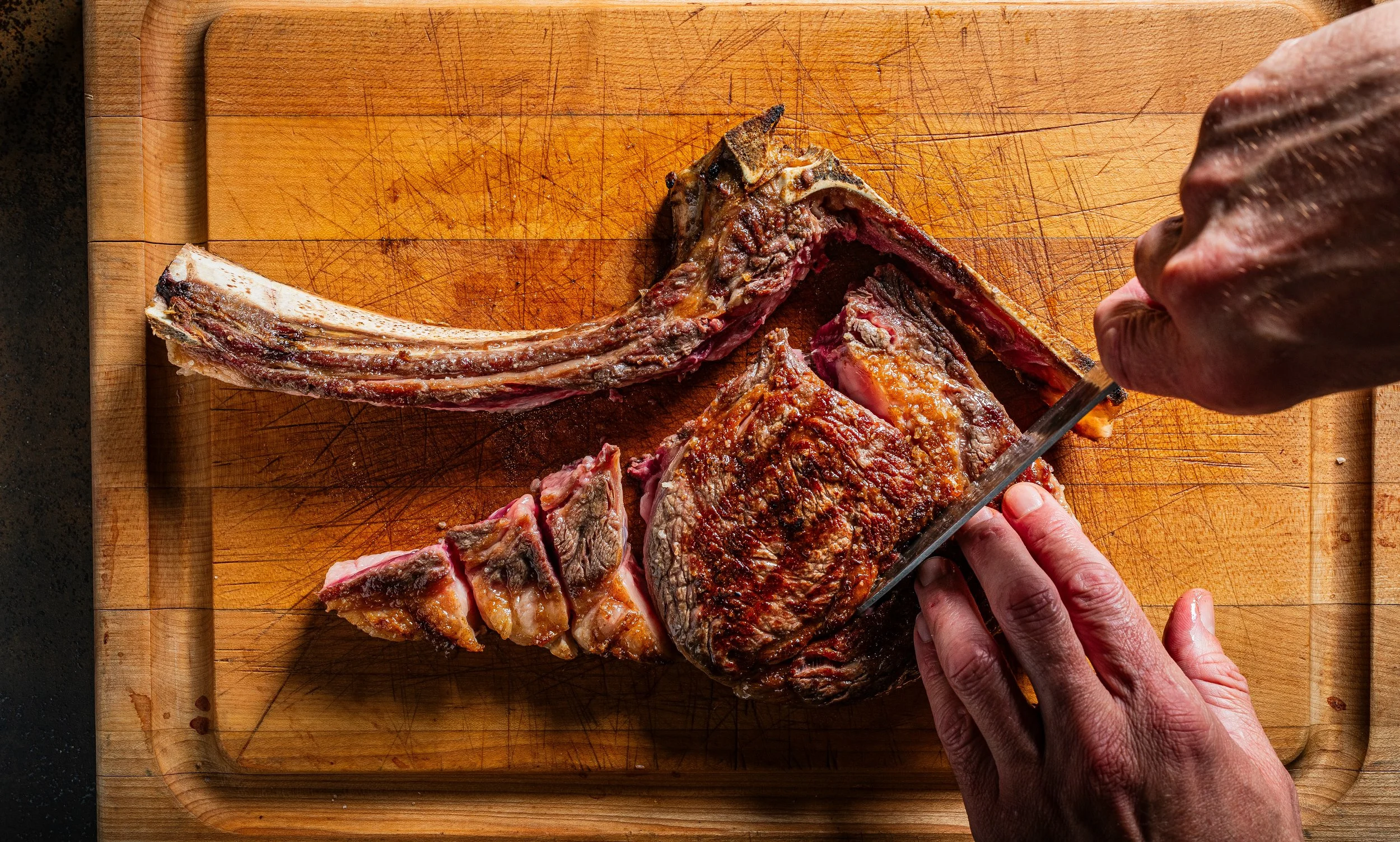 A person carving cooked meat on a wooden cutting board.