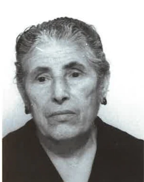 Black and white portrait of an elderly woman with slicked back hair, wearing earrings and a dark top.