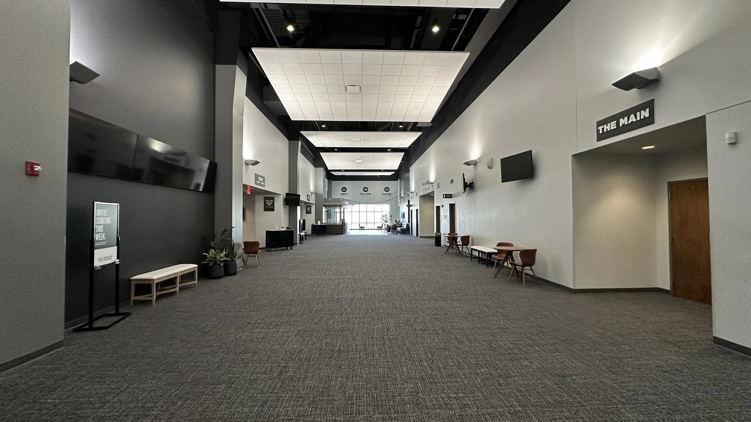 Empty hallway with seating, wall-mounted screens, and signage indicating different areas of a public building or conference center.