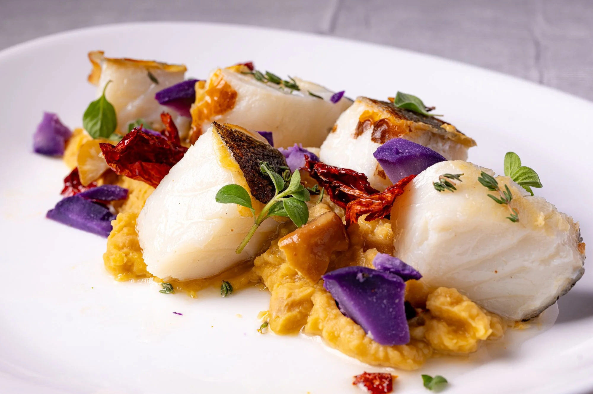 Piatto di baccalà, contorno di purè di ceci, patate viola e alcune foglie di basilico.