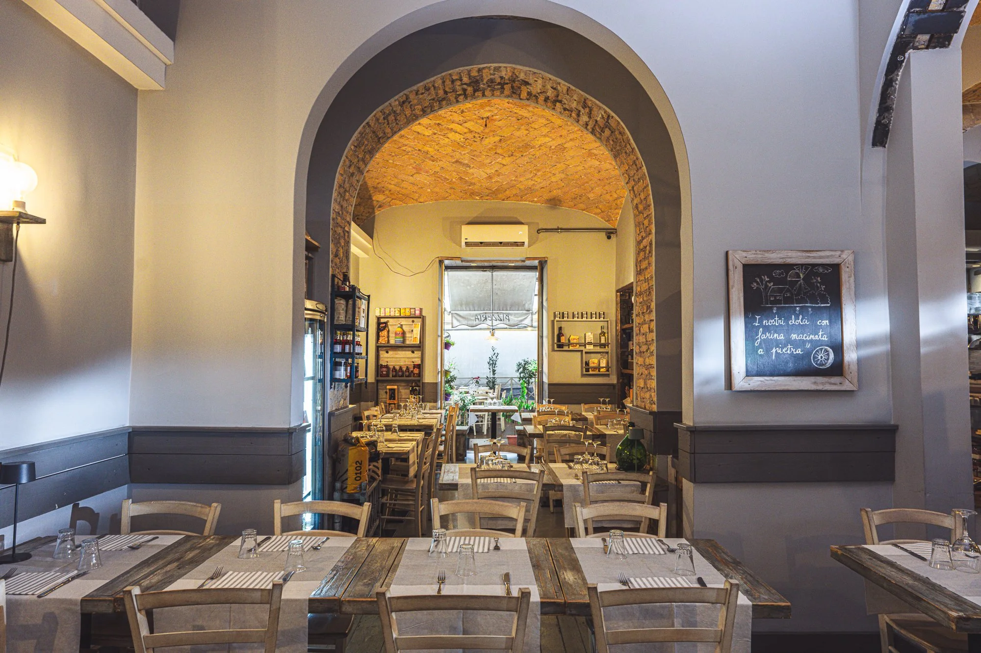 Interno di un ristorante con tavoli apparecchiati e un arco in mattoni che conduce a una terrazza luminosa.