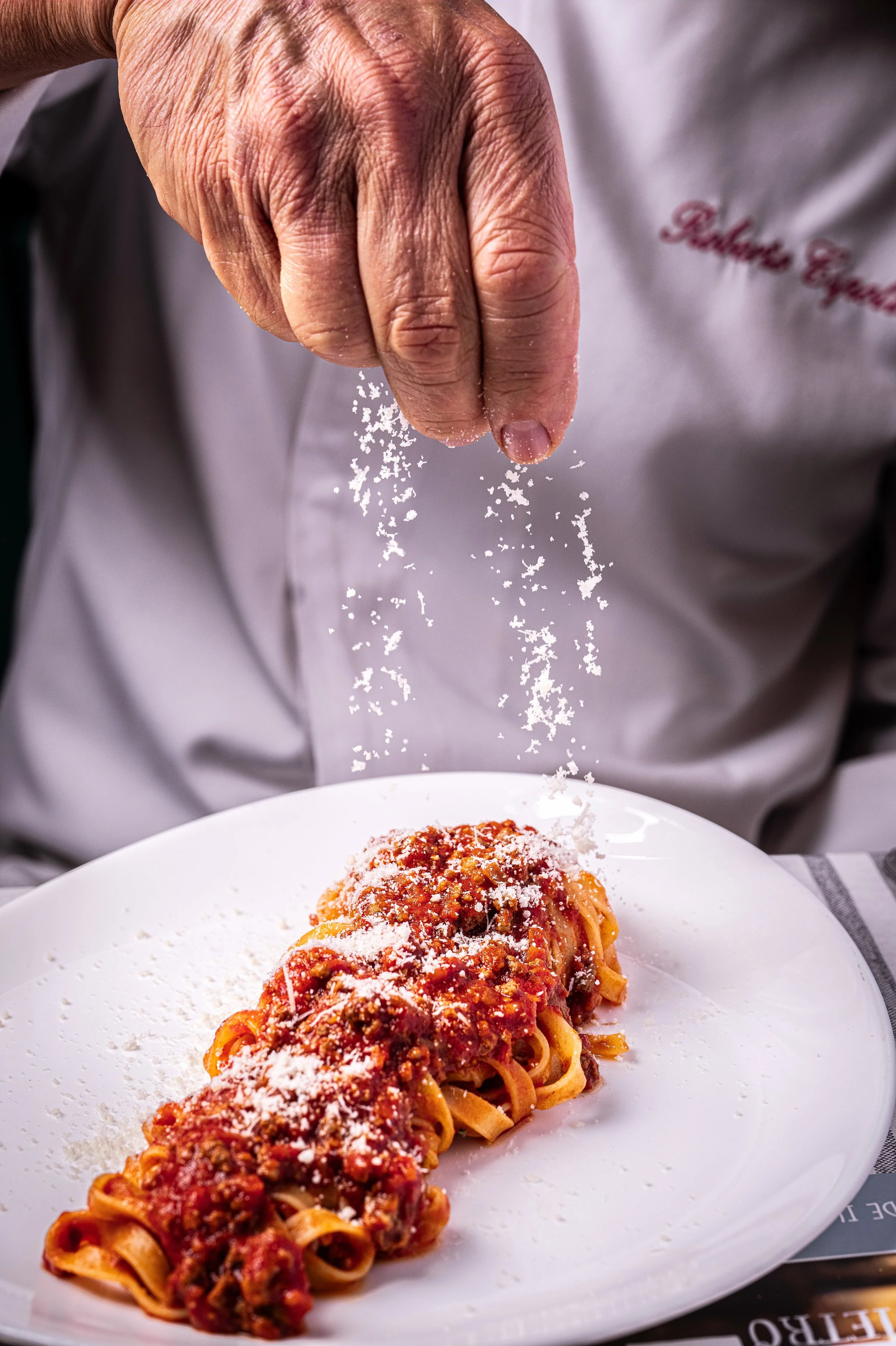 Uno chef versa del Parmigiano Reggiano grattugiato su un piatto di tagliatelle al ragù.