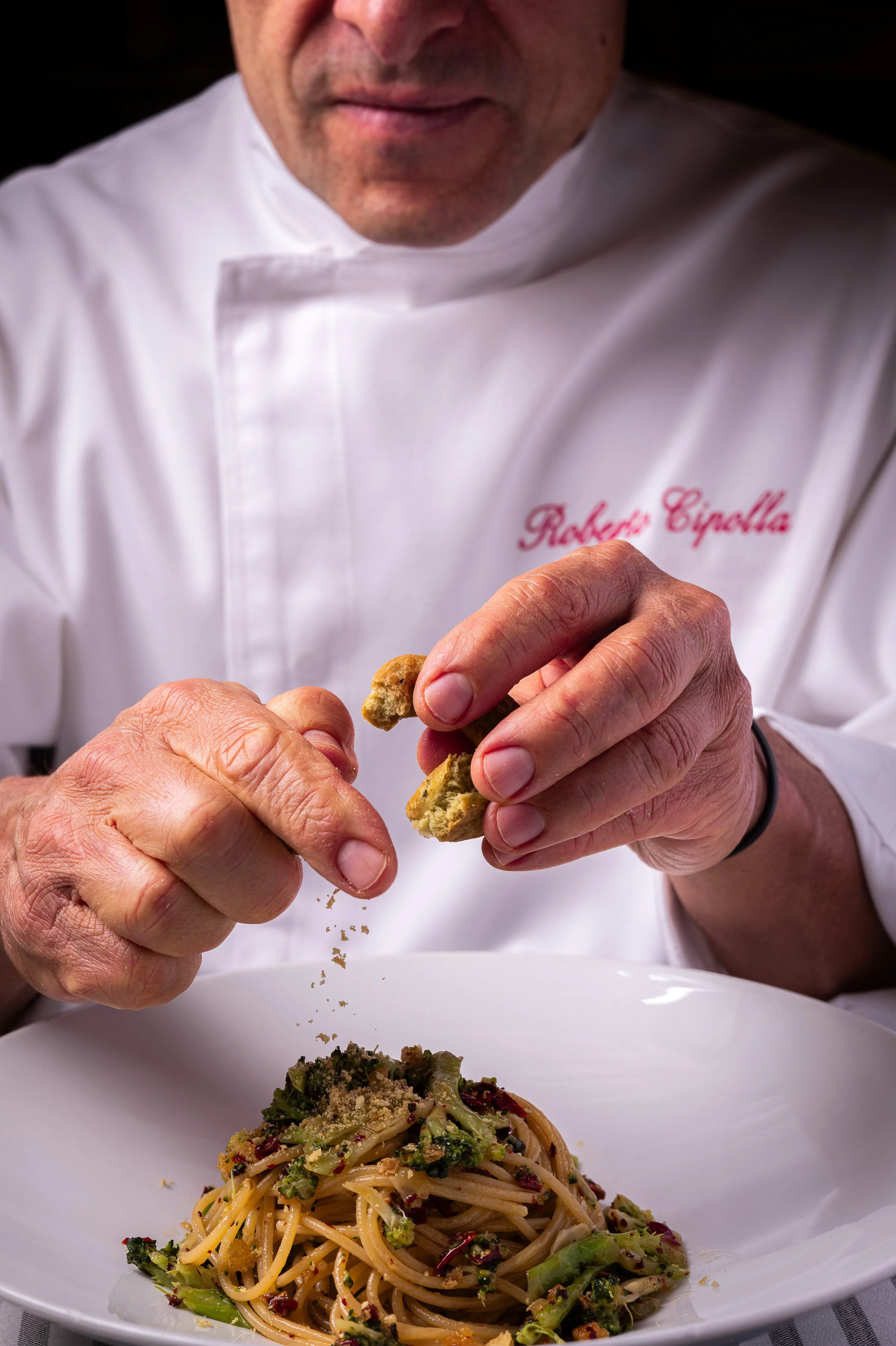 Chef che condisce un piatto di pasta con tarallo sbriciolato.