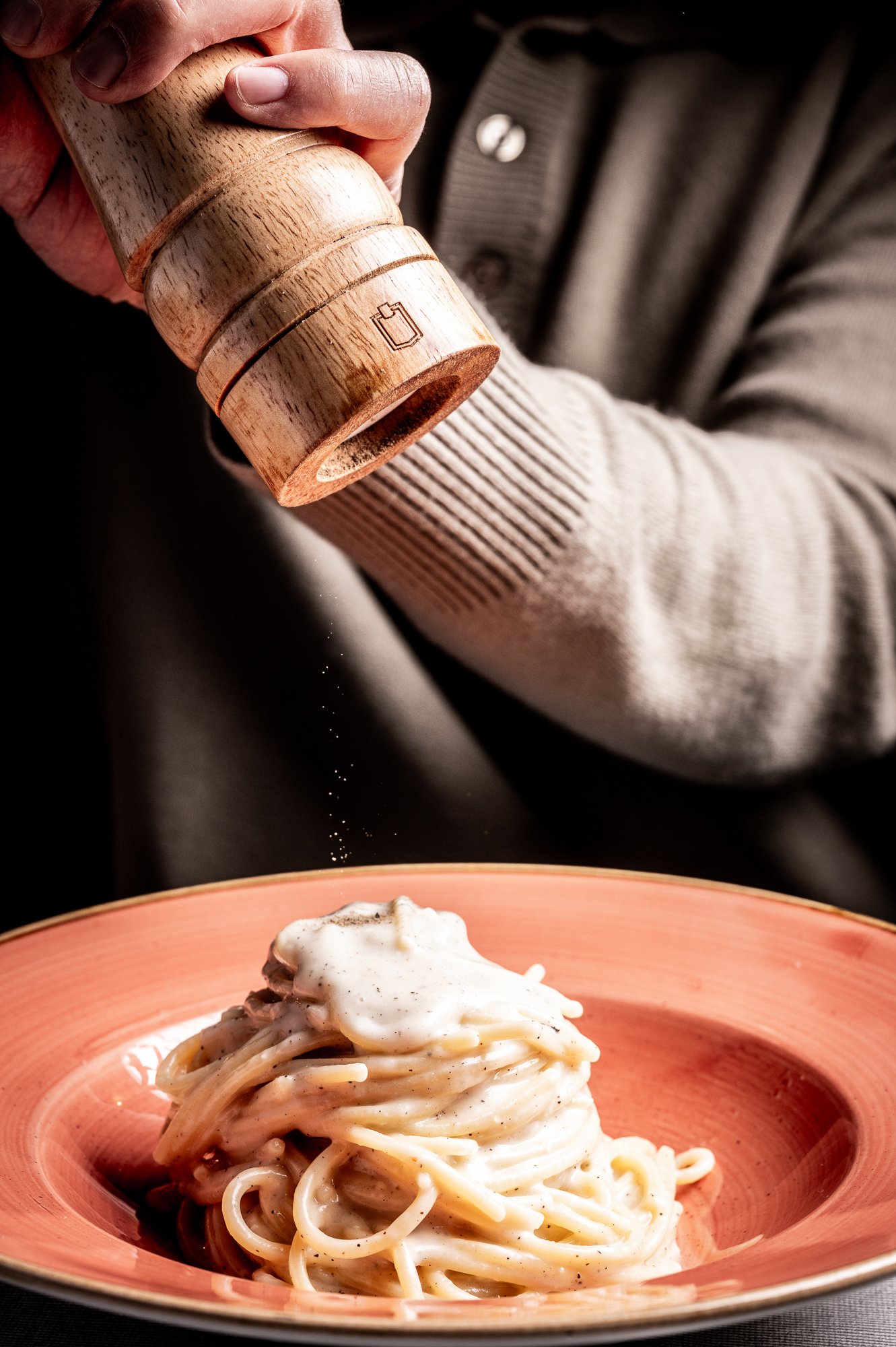 Una mano sta pepando un piatto di spaghetti cacio e pepe.