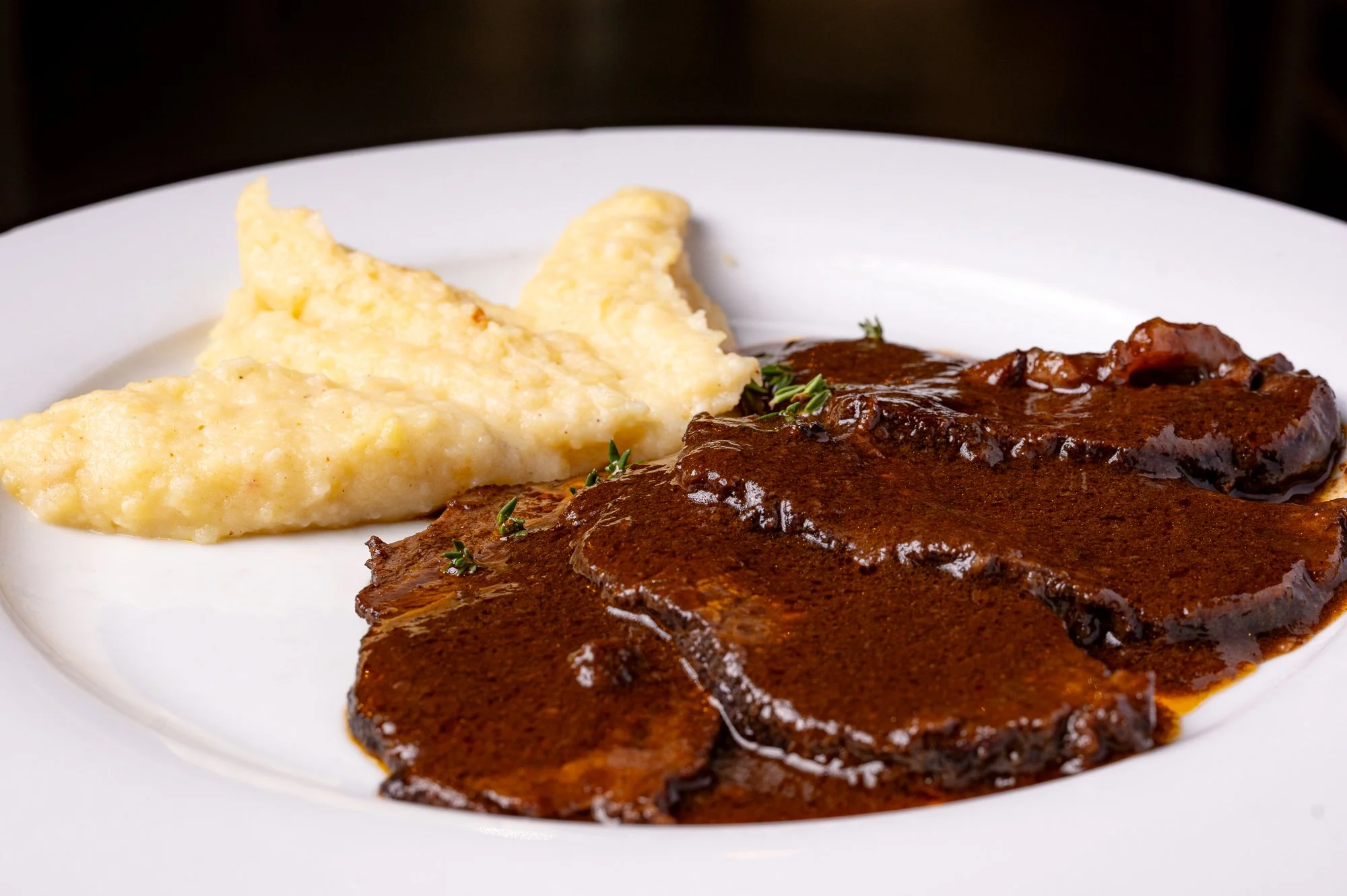 Guancia di manzo con salsa al vino rosso, purè di patate sulla sinistra.