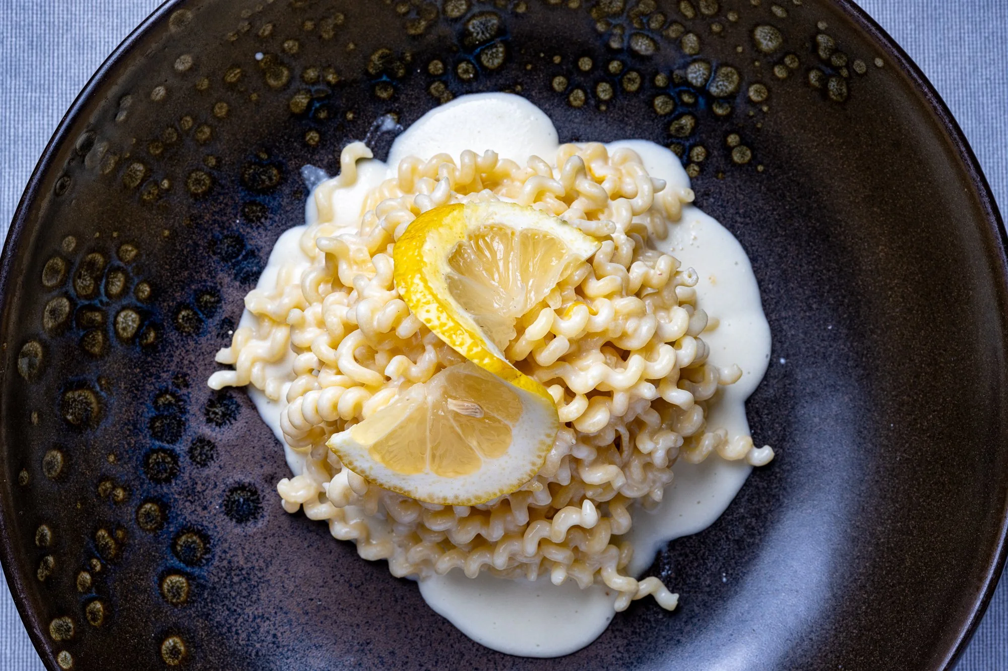 Pasta 'riccioli' con salsa bianca e fettine di limone in un piatto di ceramica scura.