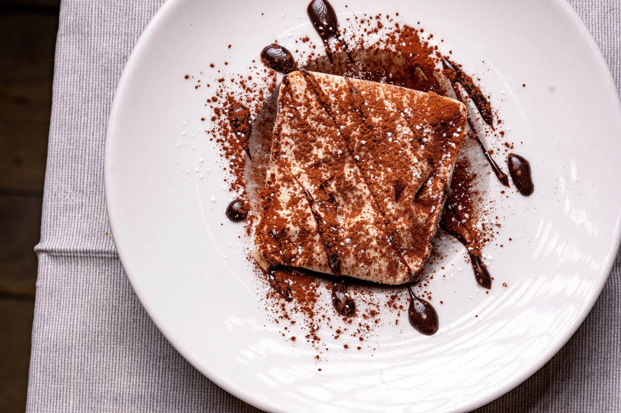 Tartufo di pizzo con cacao in polvere e decorazioni di cioccolato su piatto bianco.