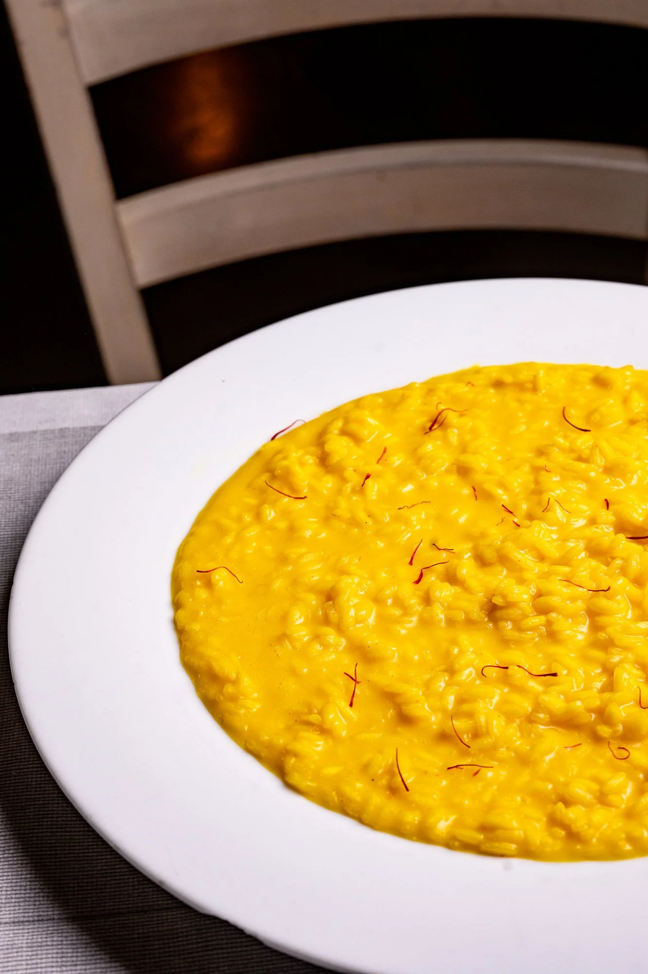 Risotto allo zafferano servito in un piatto bianco, decorato con fili di zafferano.