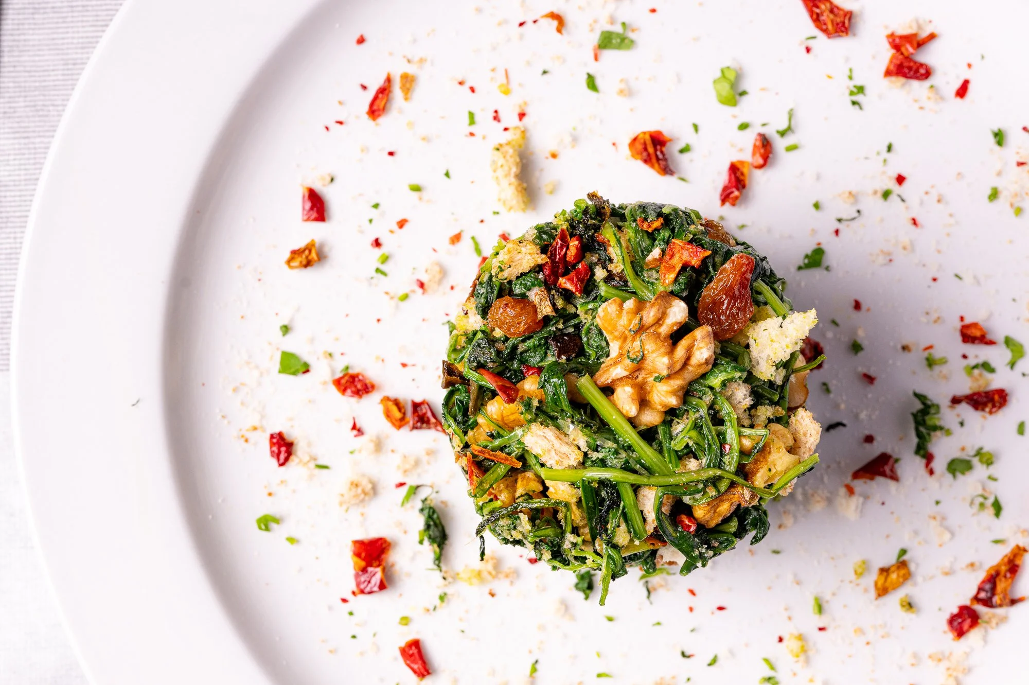 Piatto di cicoria ripassata, decorato con peperoncino rosso e erbe aromatiche, su un piatto bianco.