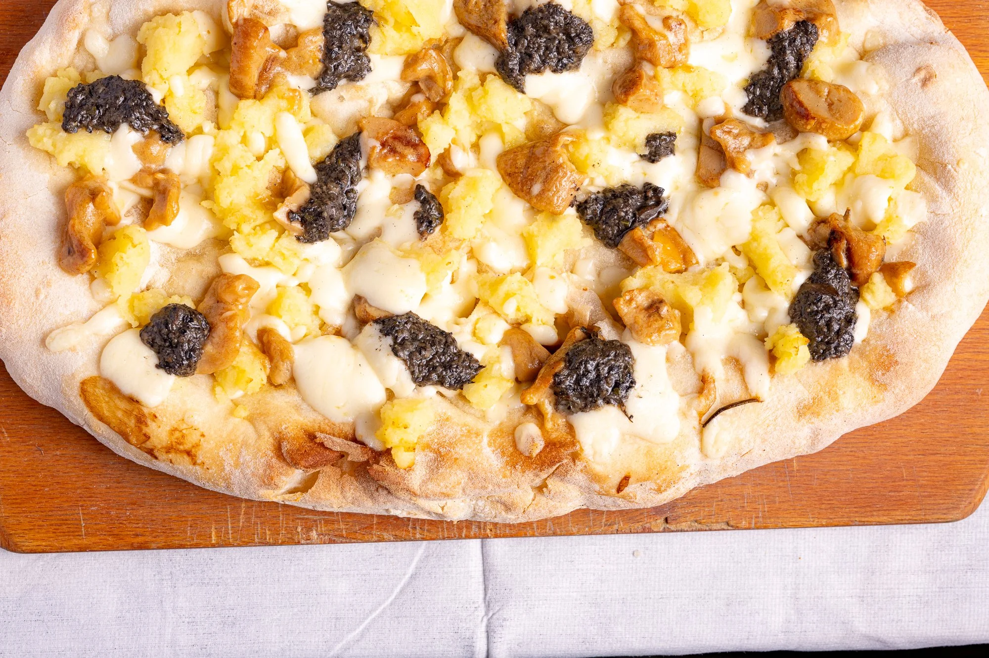 Pizza con patate, mozzarella, funghi e salsa tartufata su tagliere di legno.