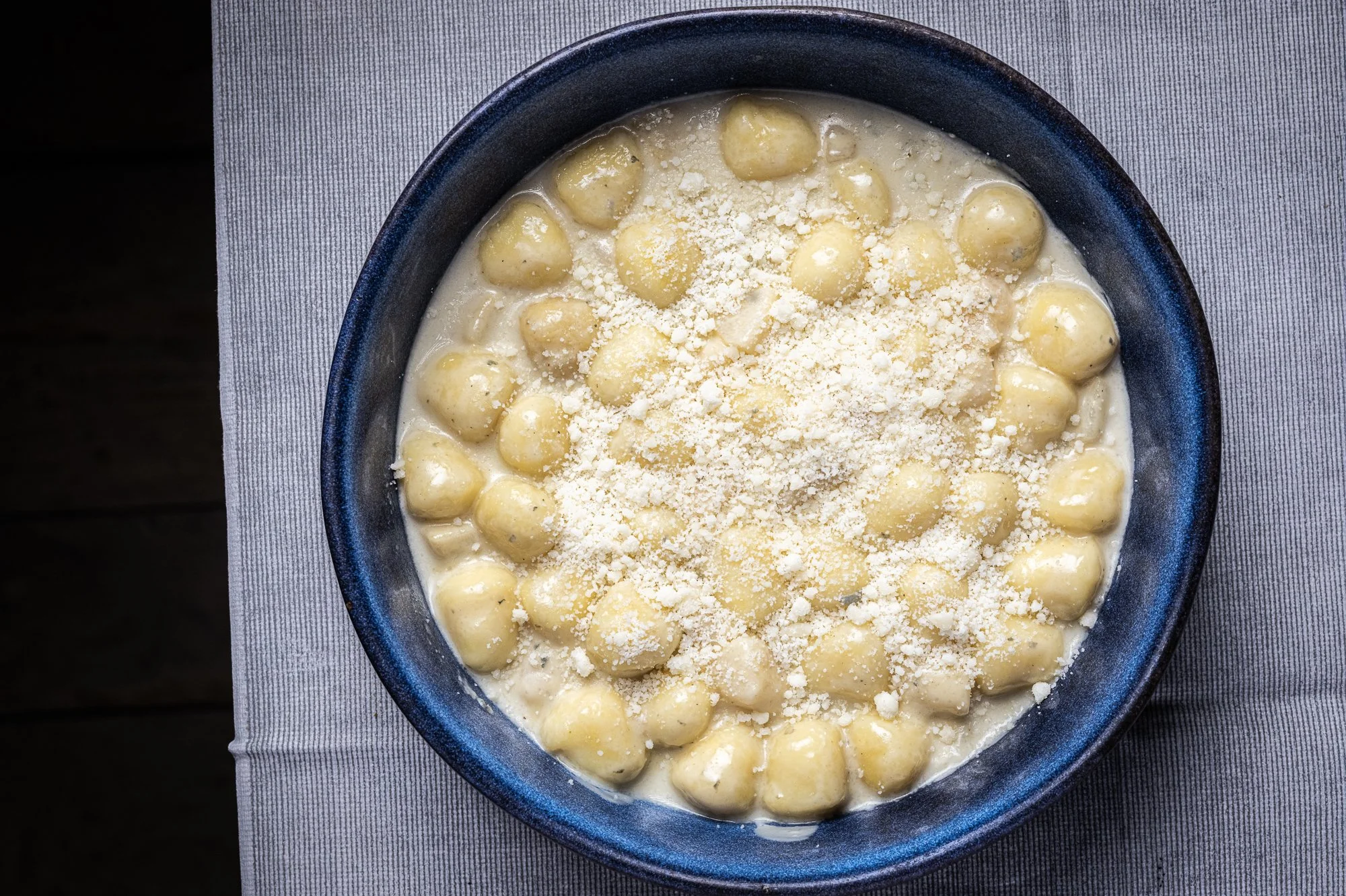 Ciotola di gnocchi di patate con salsa al gorgonzola e formaggio grattugiato sopra.