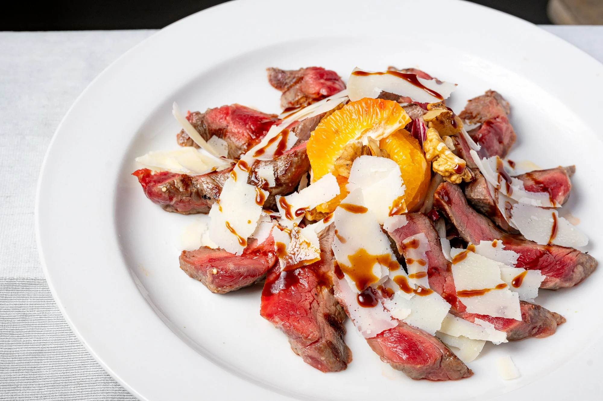 Piatti di tagliata di manzo, scaglie di Parmigiano Reggiano, fette di arancia, noci, e glassa di aceto balsamico.