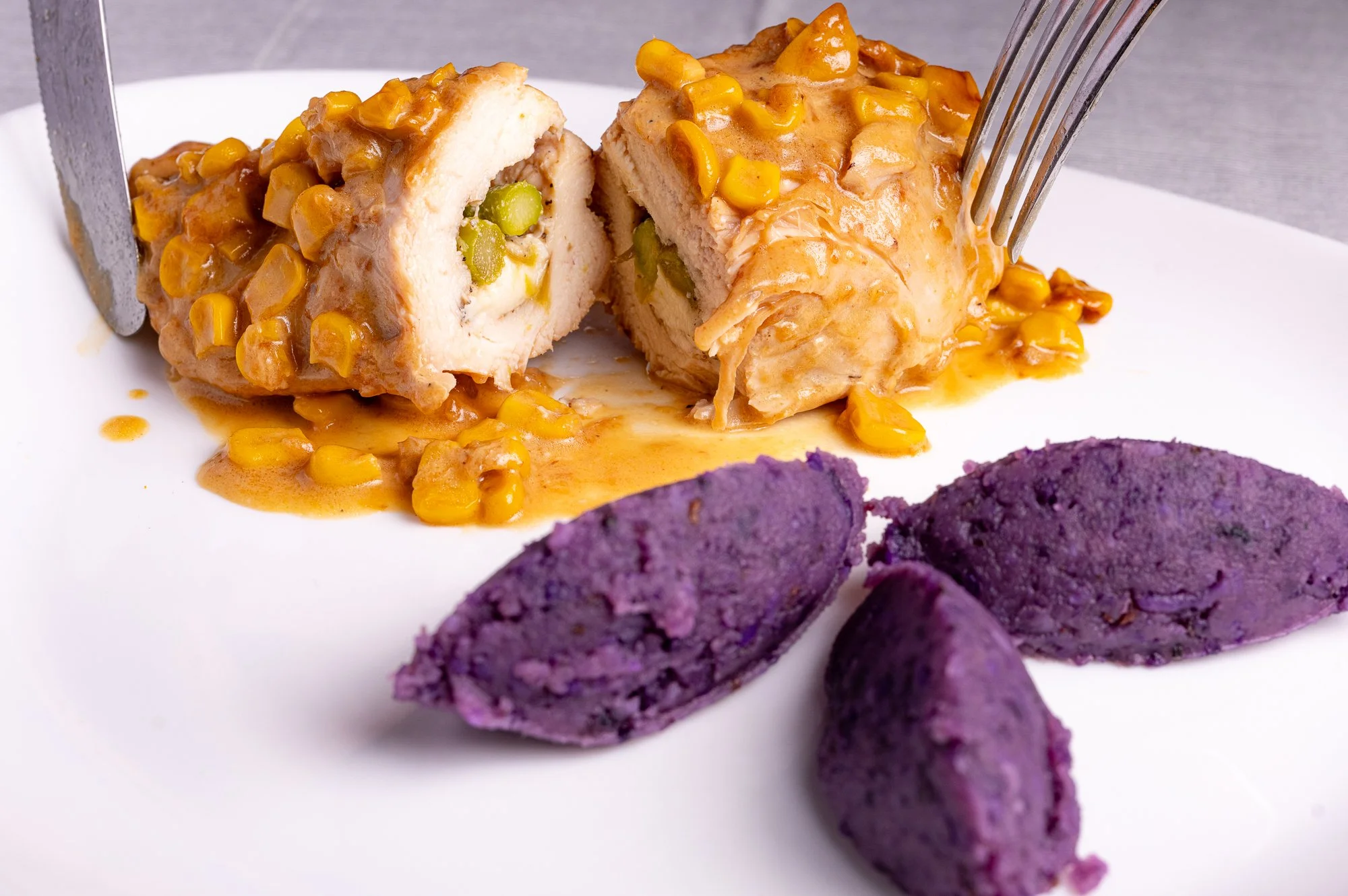 Suprema di pollo ripiena, coperta di salsa e servita con quenelle di patate viola.