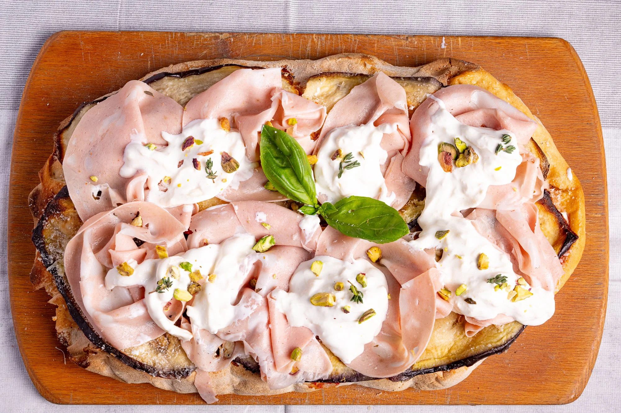 Pizza con mortadella, stracciatella, basilico e pistacchi, su tagliere di legno.