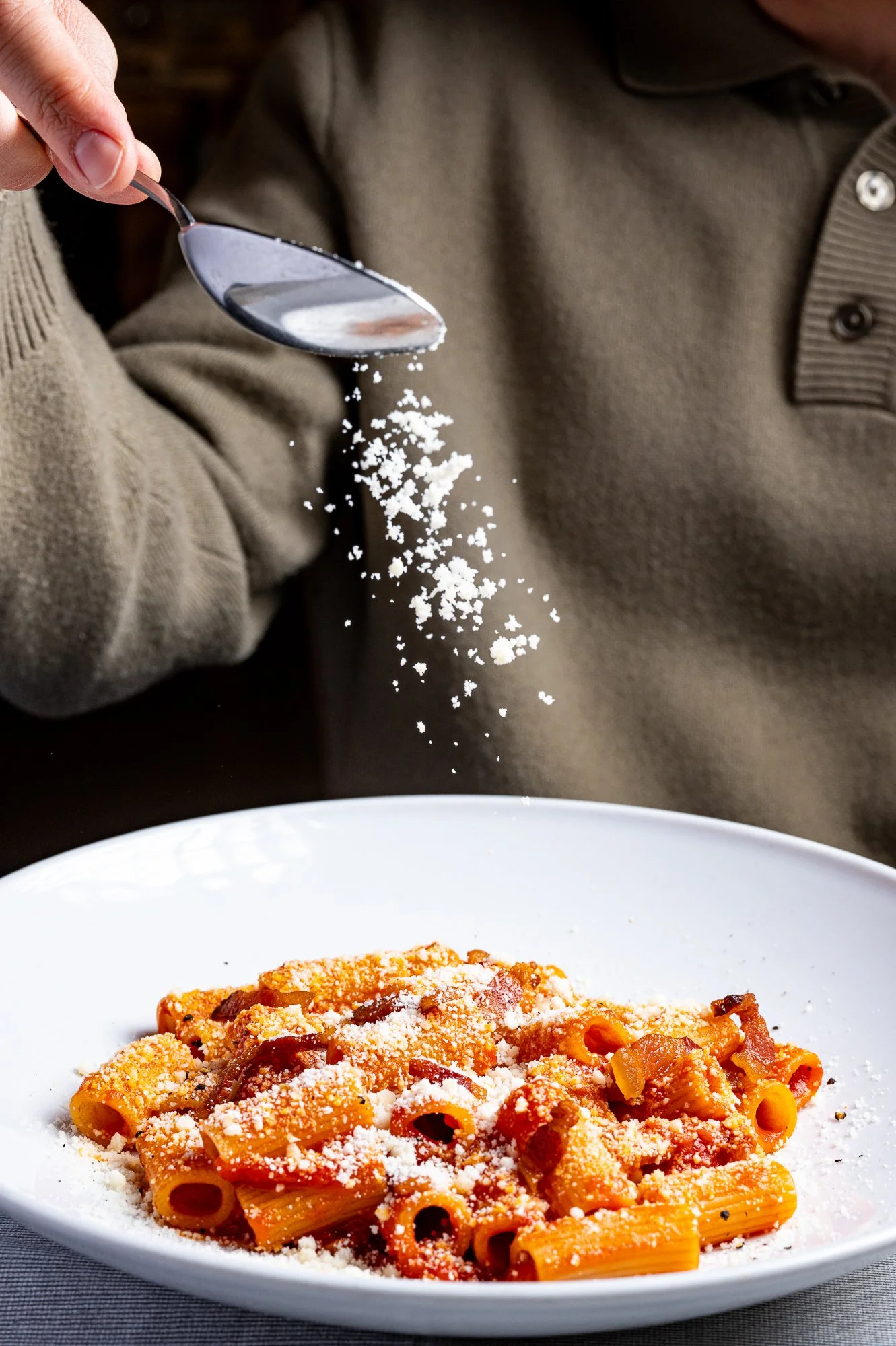 Una persona versa Pecorino Romano su un piatto di rigatoni all'amatriciana.