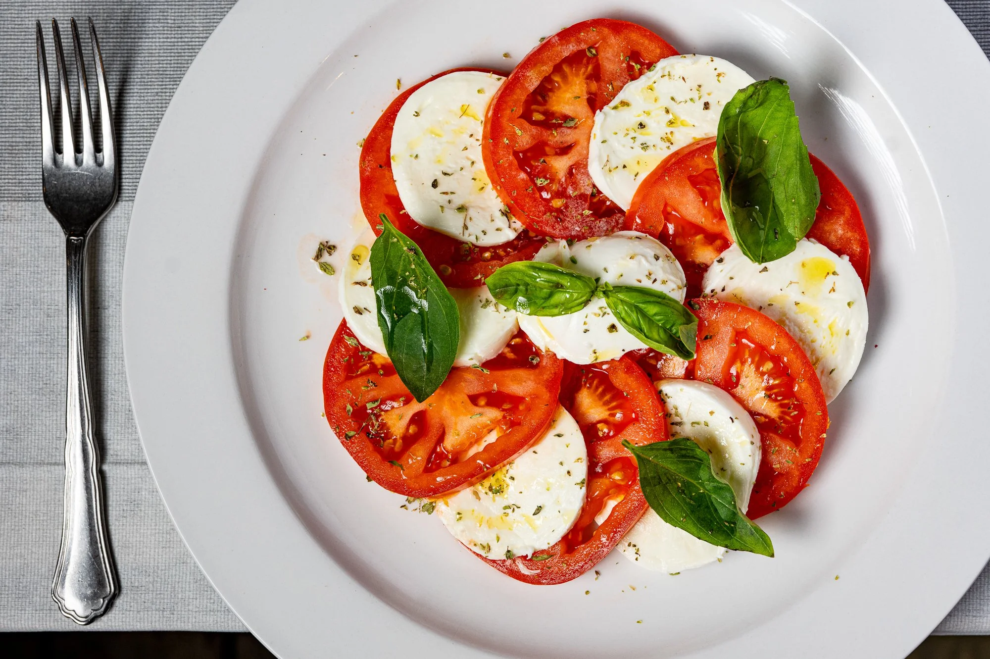 Insalata caprese su piatto bianco con pomodori, mozzarella, basilico, olio d'oliva e origano.
