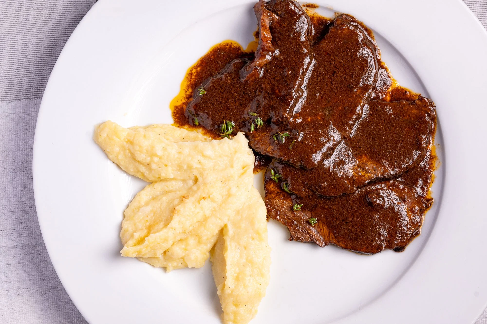Guancia di manzo con purè di patate e salsa al vino rosso, serviti su piatto bianco.
