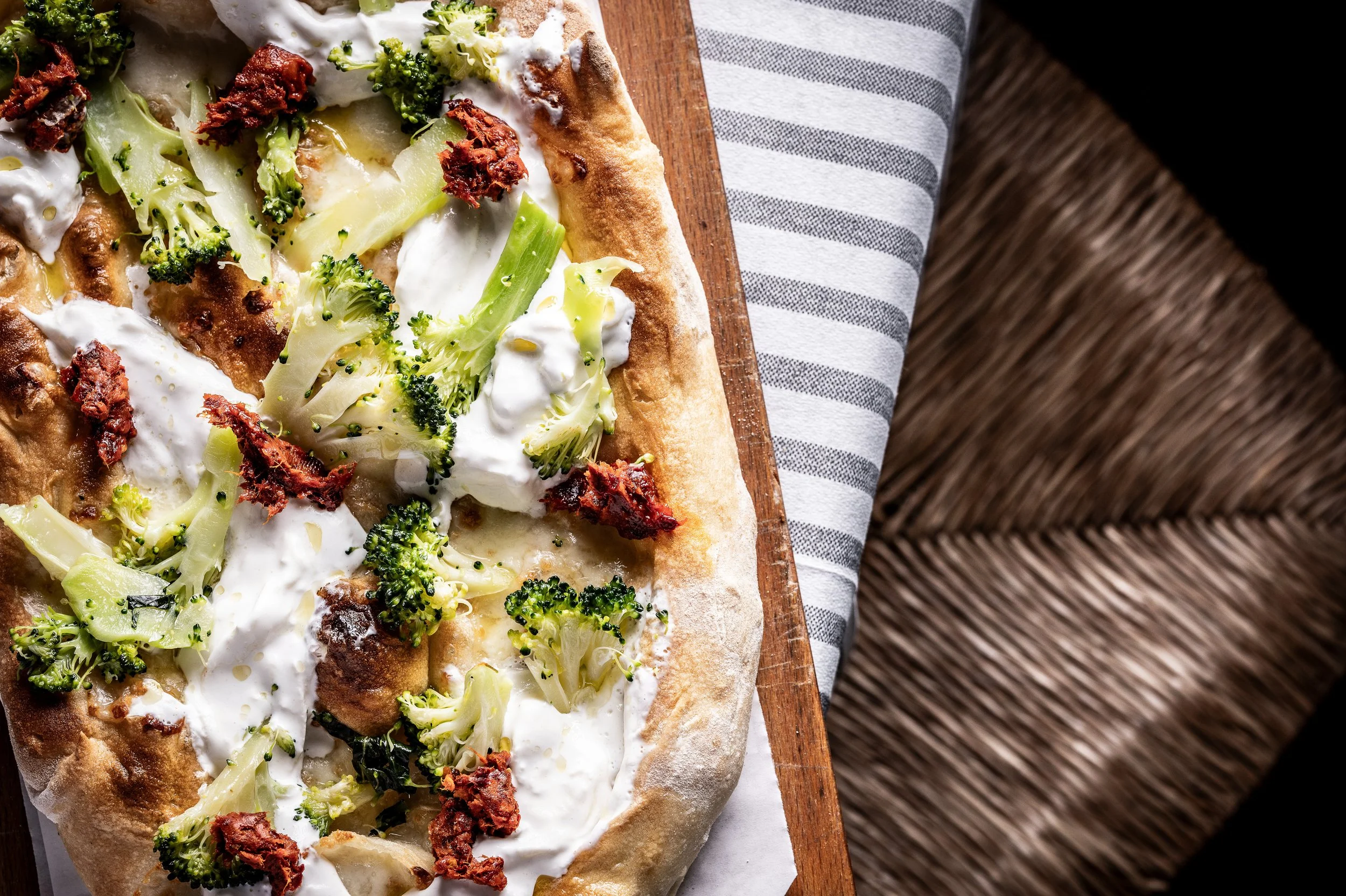 Pizza con broccoli, stracciatella e ’nduja su un tagliere di legno.