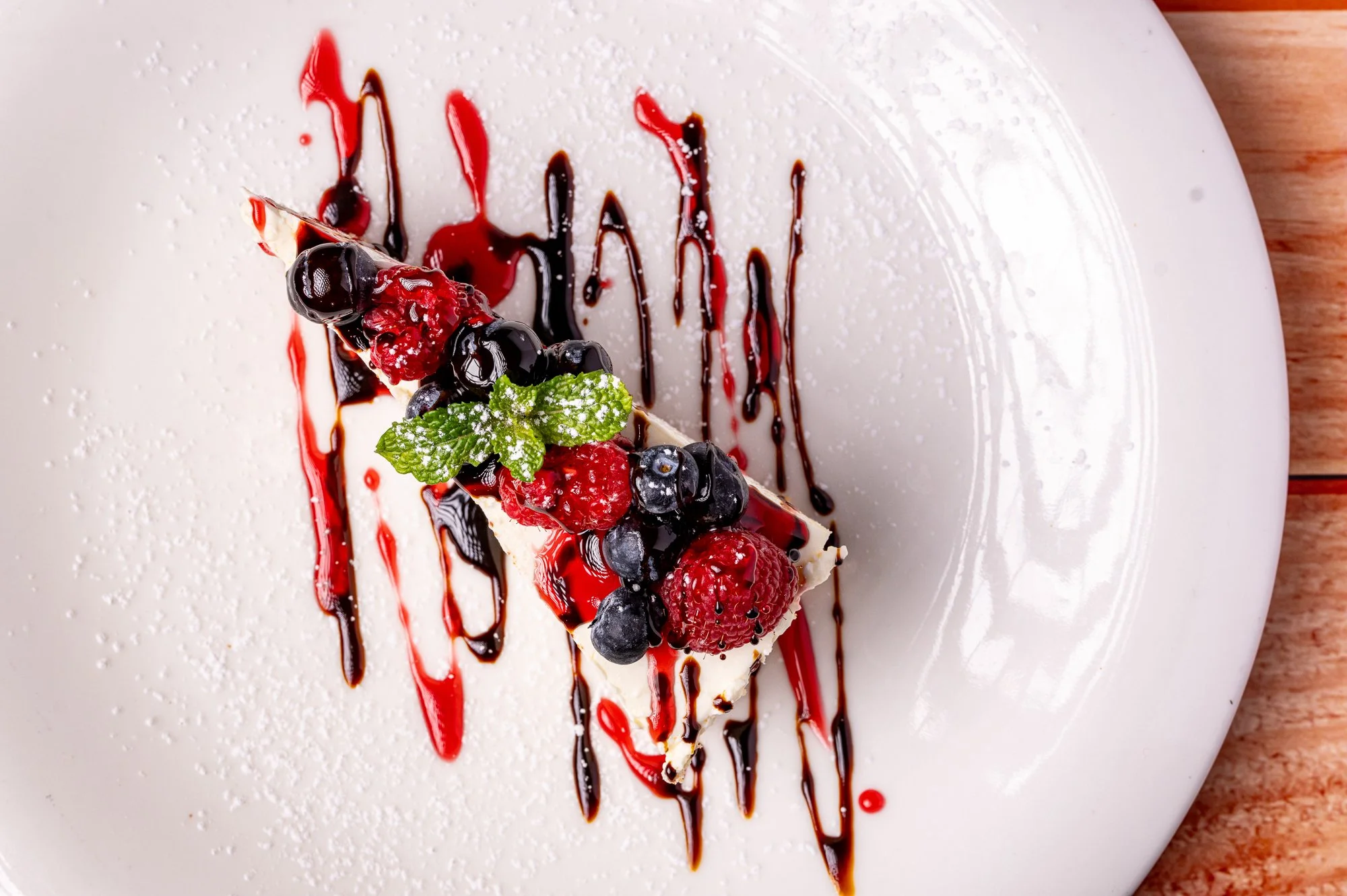 Torta cheesecake con frutti di bosco e menta decorata con sciroppo di cioccolato e frutti di bosco su un piatto bianco