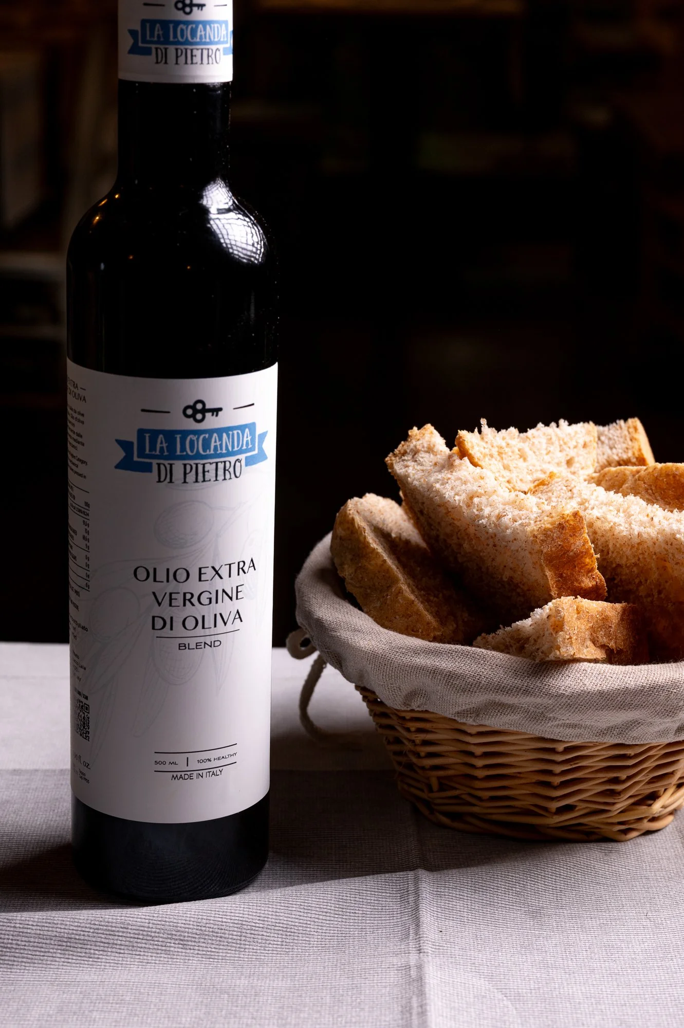 Bottiglia di olio extravergine di oliva accanto a un cestino di pane.