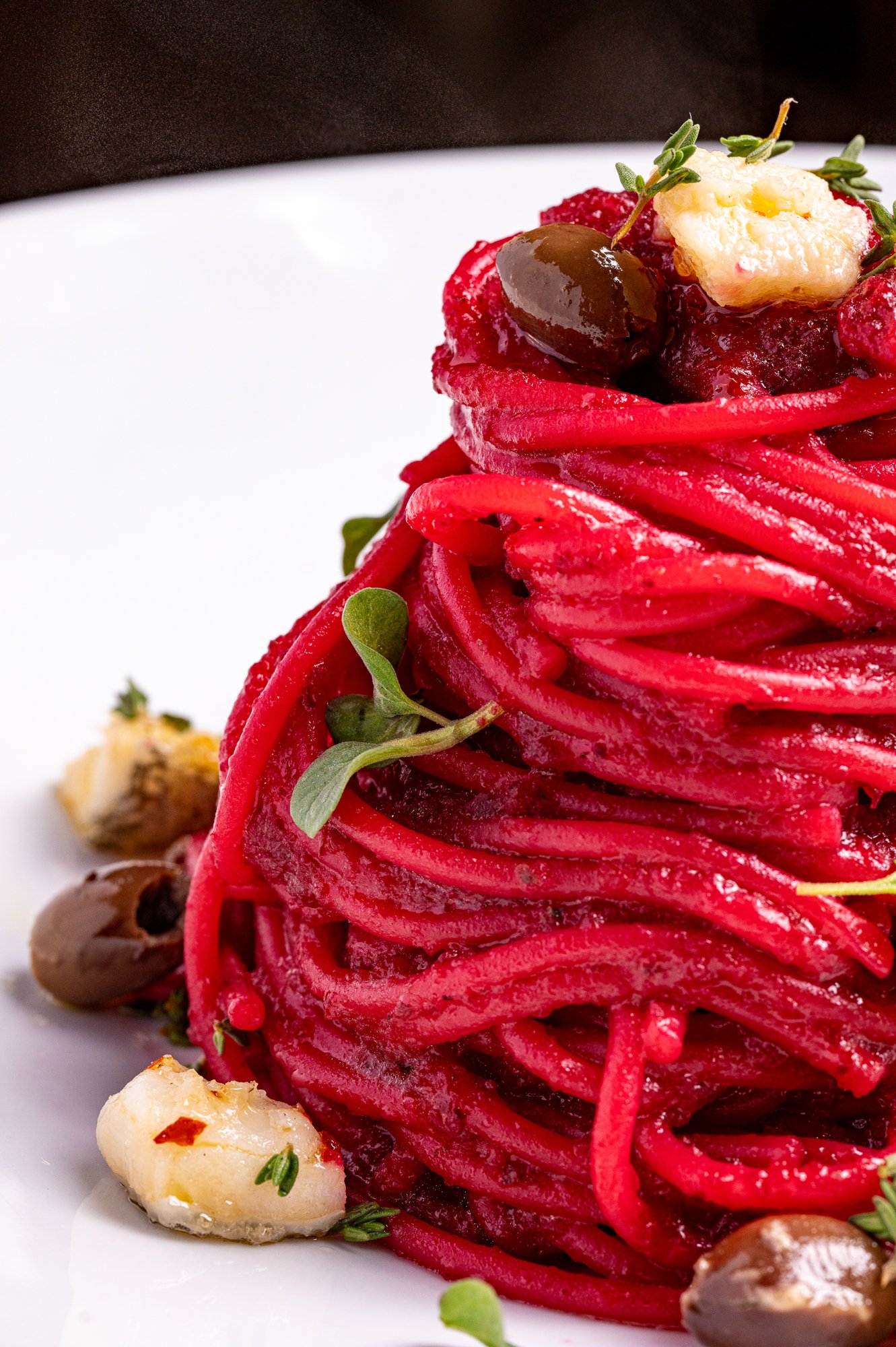 Pasta alla barbabietola rossa con baccala, olive e erbe fresche, vista in primo piano.