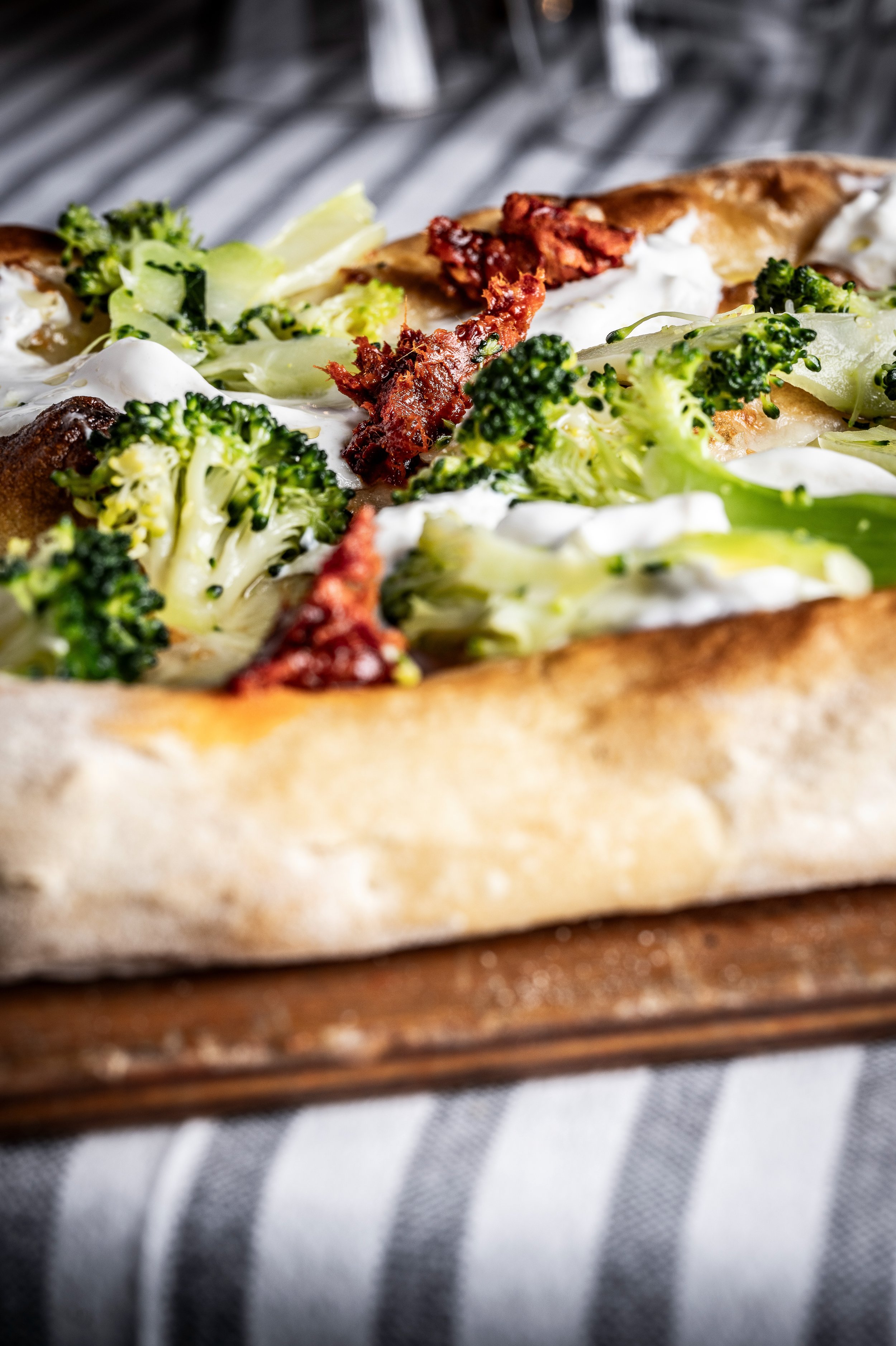 Pizza con broccoli, stracciatella e ’nduja su un tagliere di legno, vista di lato.