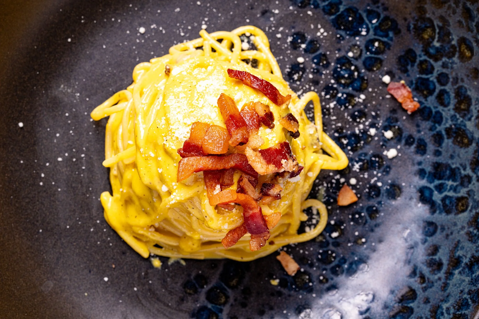 Spaghetti alla carbonara con guanciale, Pecorino Romano e pepe, serviti in un piatto nero, visti dall'alto.