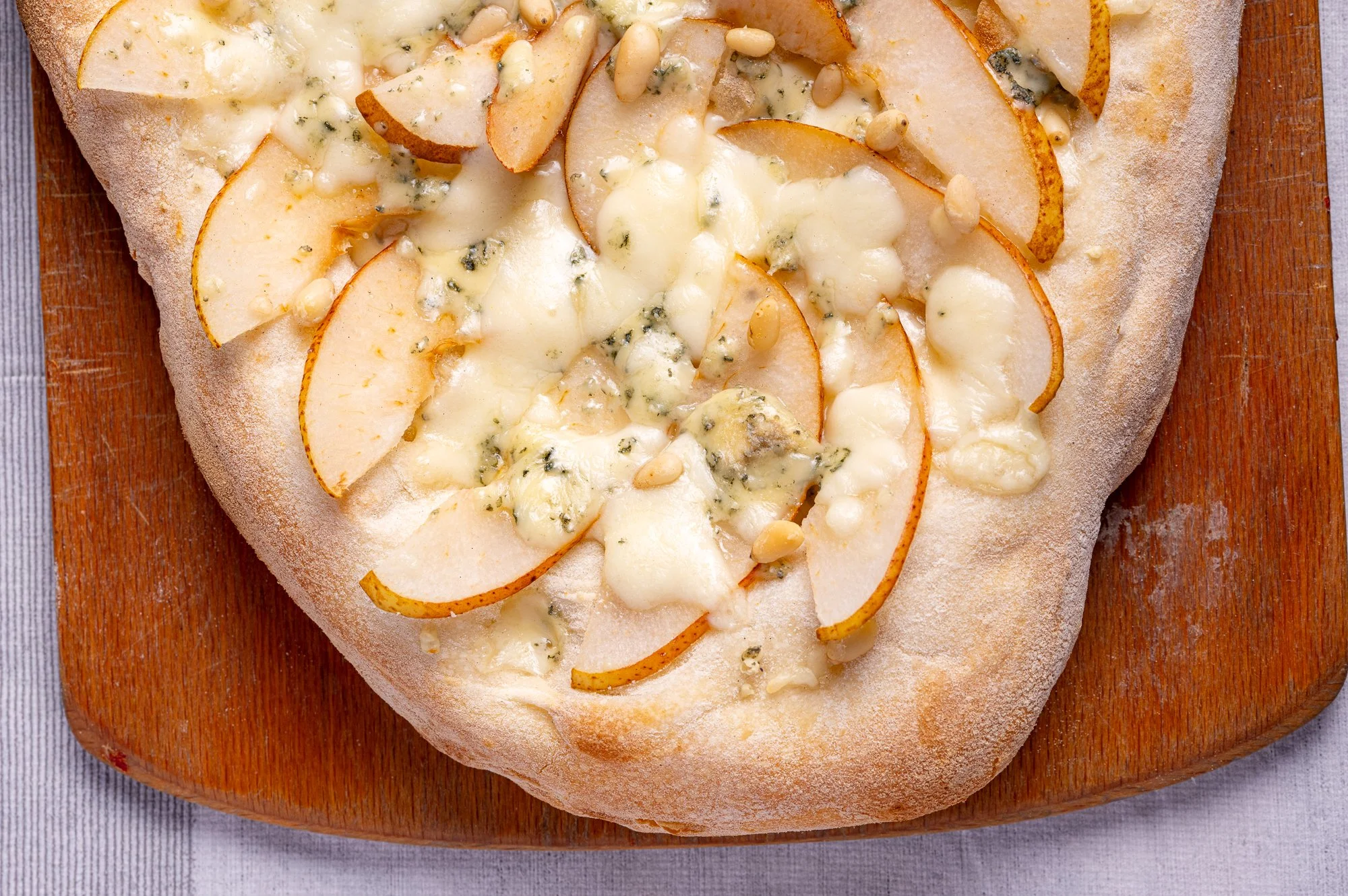 Pizza con pere, gorgonzola e pinoli, su tagliere di legno.