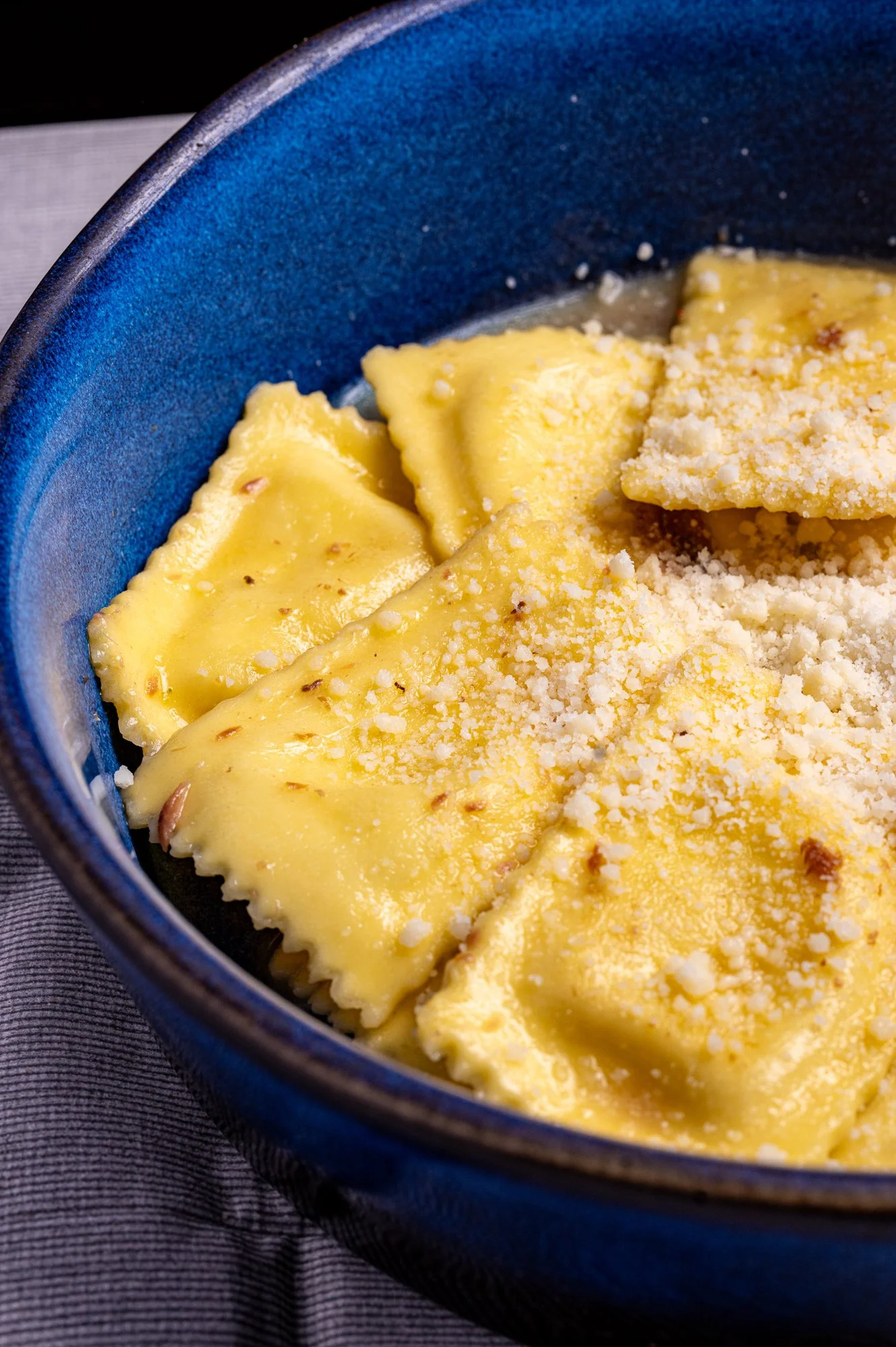 Ravioli con salsa e formaggio grattugiato in una ciotola blu.