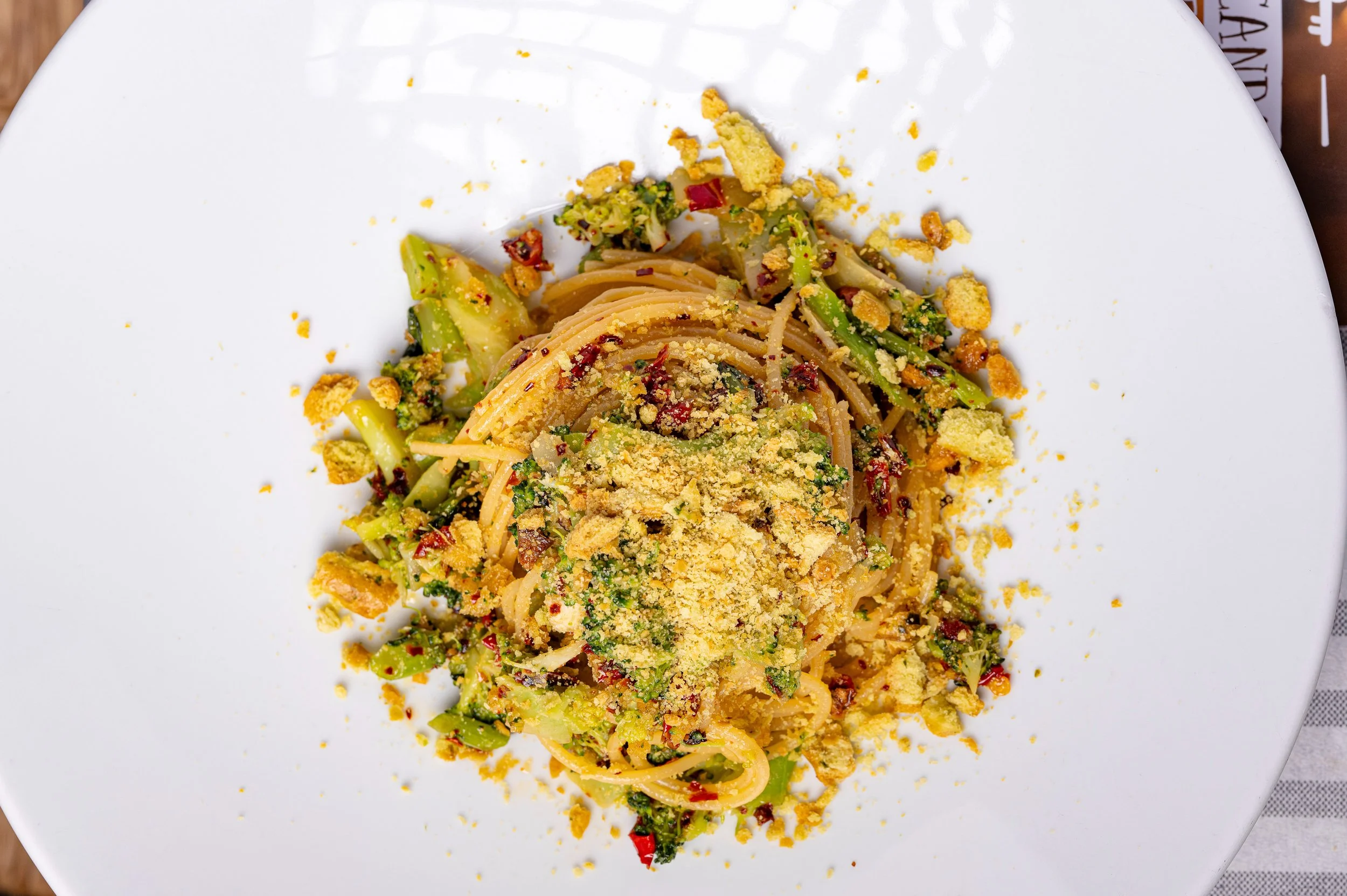 Piatto di spaghetti con verdure e condimenti, decorato con tarallo sbriciolato.