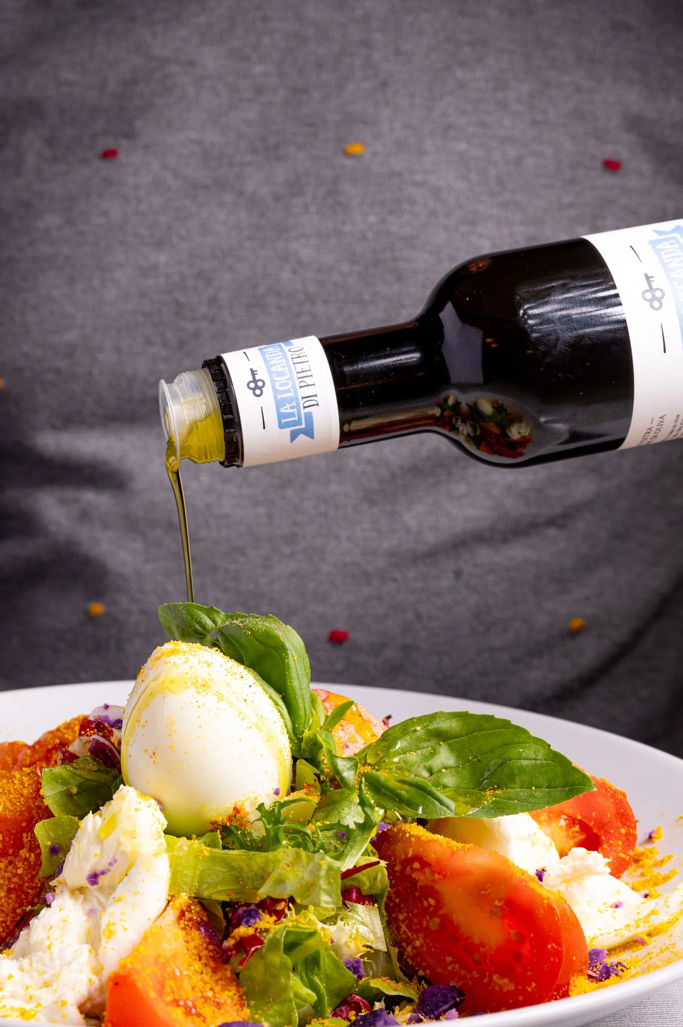 Insalata con uova, pomodori, basilico e altre verdure, con una bottiglia di olio EVO sopra.