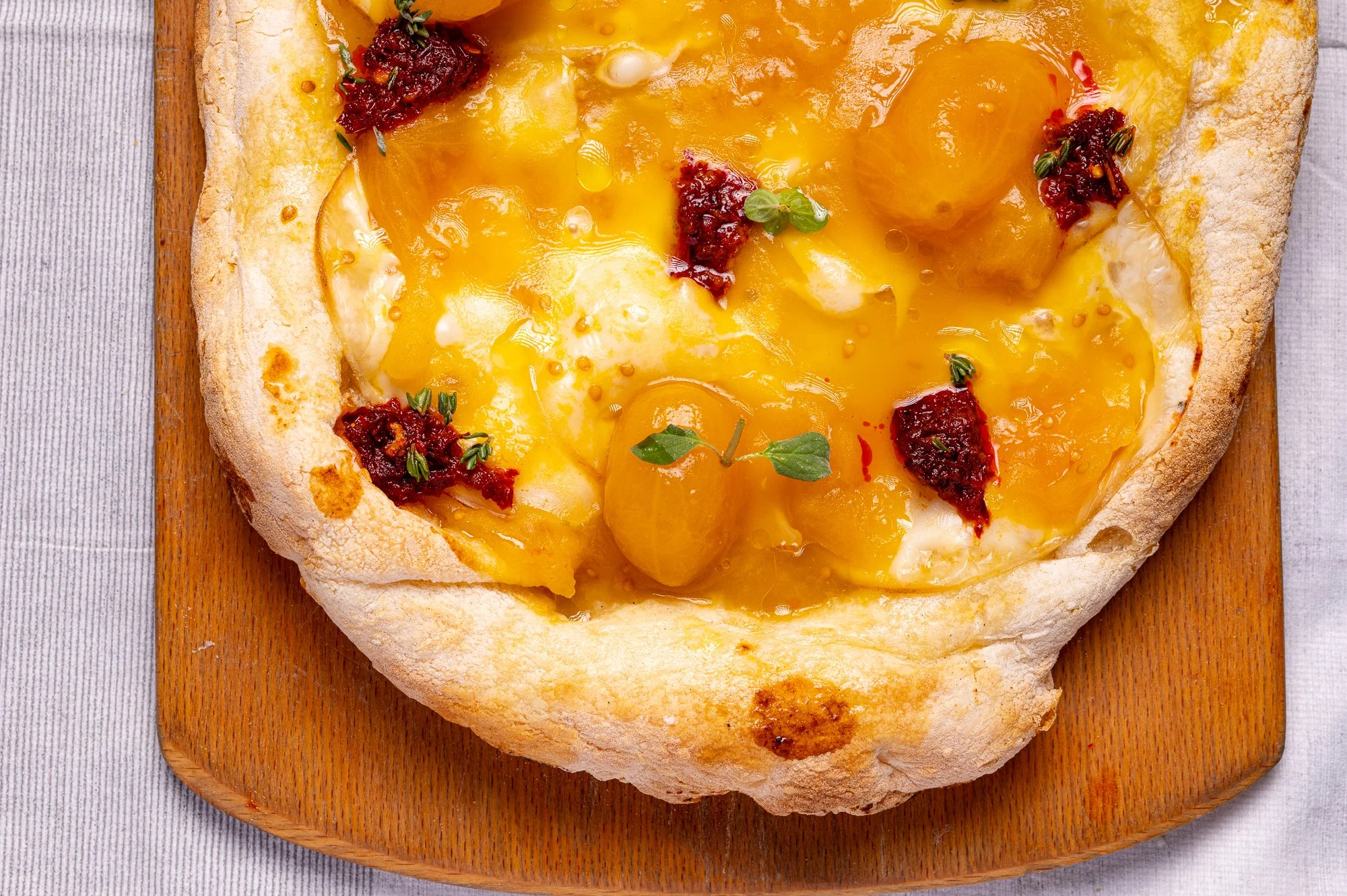 Pizza bianca con salsa di pomodorino giallo e 'nduja, decorata con erbe aromatiche, su un tagliere di legno.