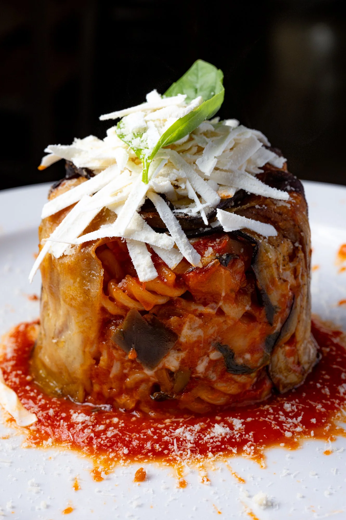 Porzione di timballo di melanzane decorata con ricotta salata e una foglia di basilico.