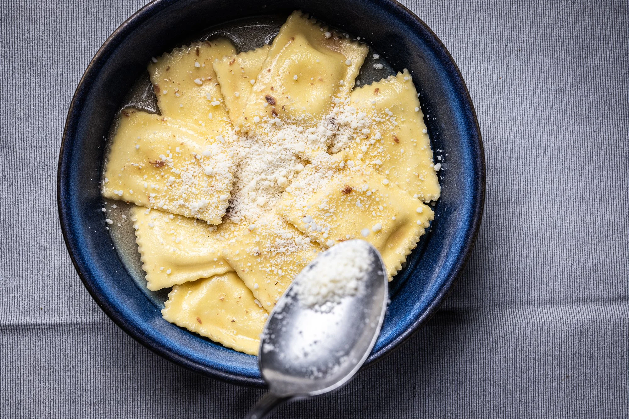 Ravioli di pasta fresca con ripieno di burrata serviti nel piatto con una spolverata di formaggio grattugiato.