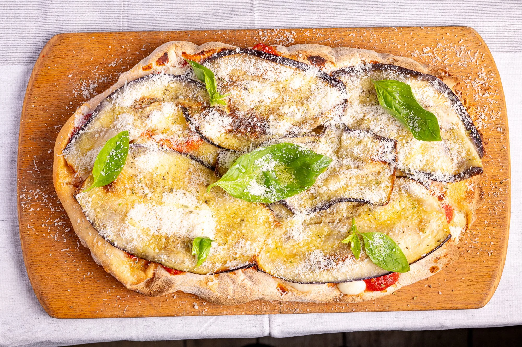 Pizza con melanzane, pomodoro, mozzarella, basilico e parmigiano su un tagliere di legno