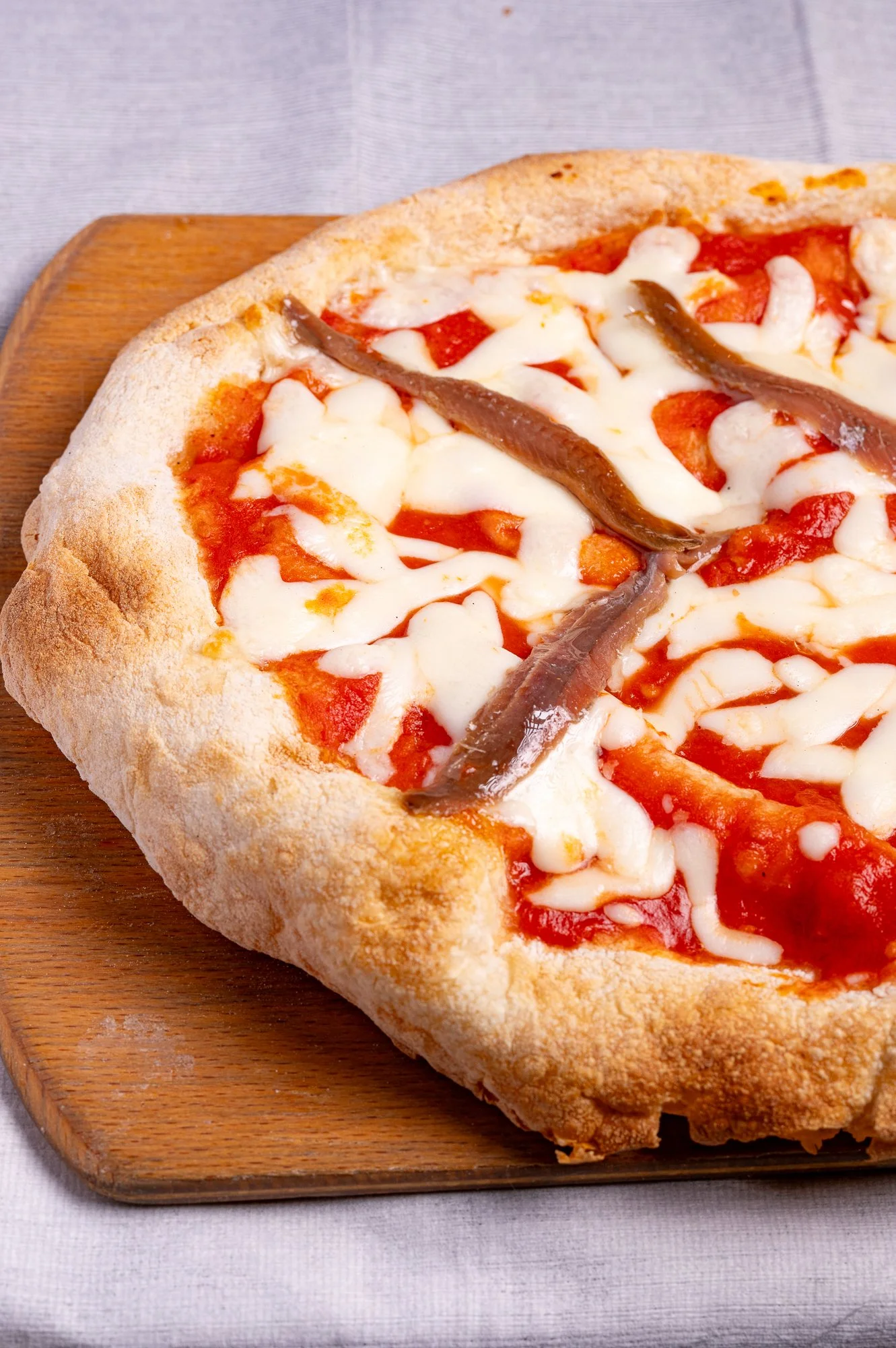 Pizza con pomodoro, mozzarella e acciughe, servita su un tagliere di legno.