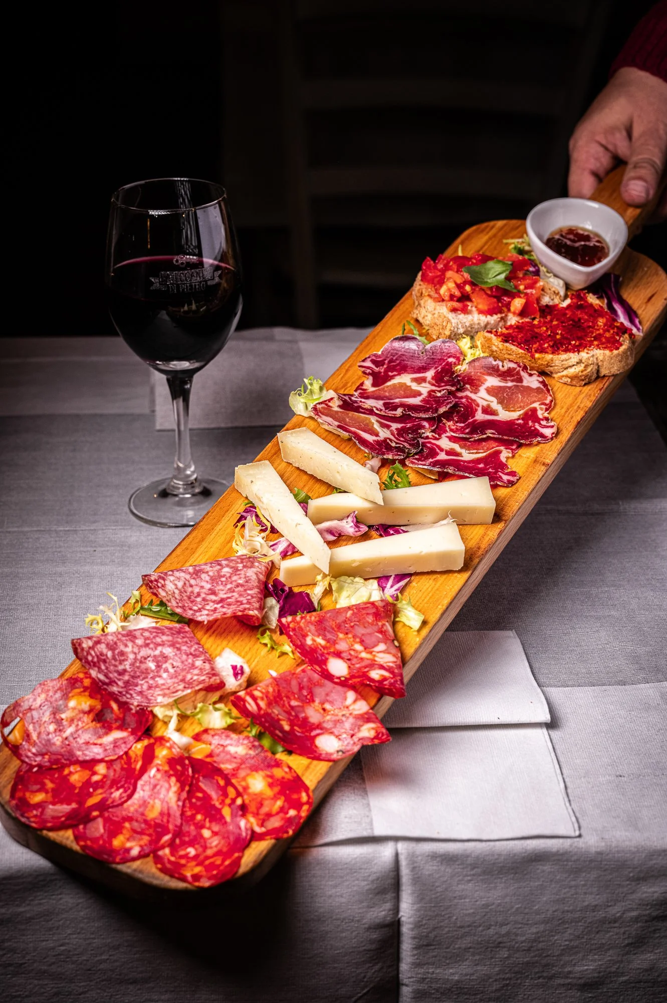 Tagliere di salumi e formaggi con un bicchiere di vino rosso
