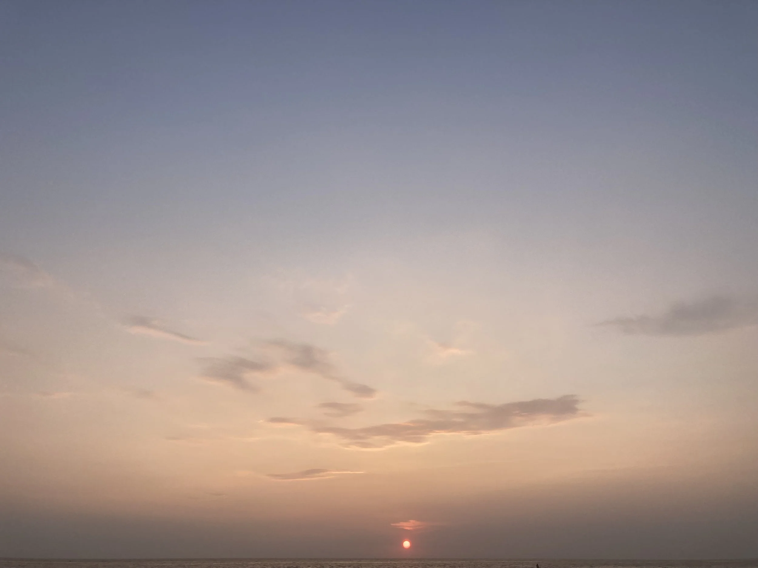 Atardecer con el sol cerca del horizonte, cielo con nubes dispersas y colores pastel en el cielo sobre el mar.