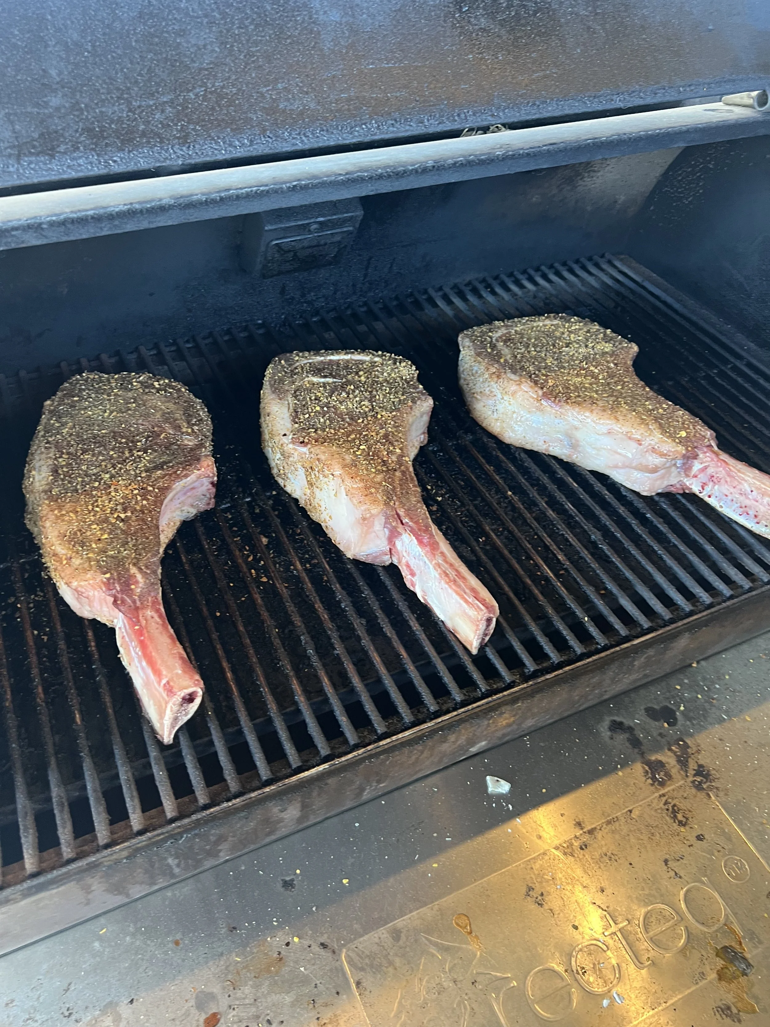 Three seasoned pork chops cooking on a grill inside a smoker.