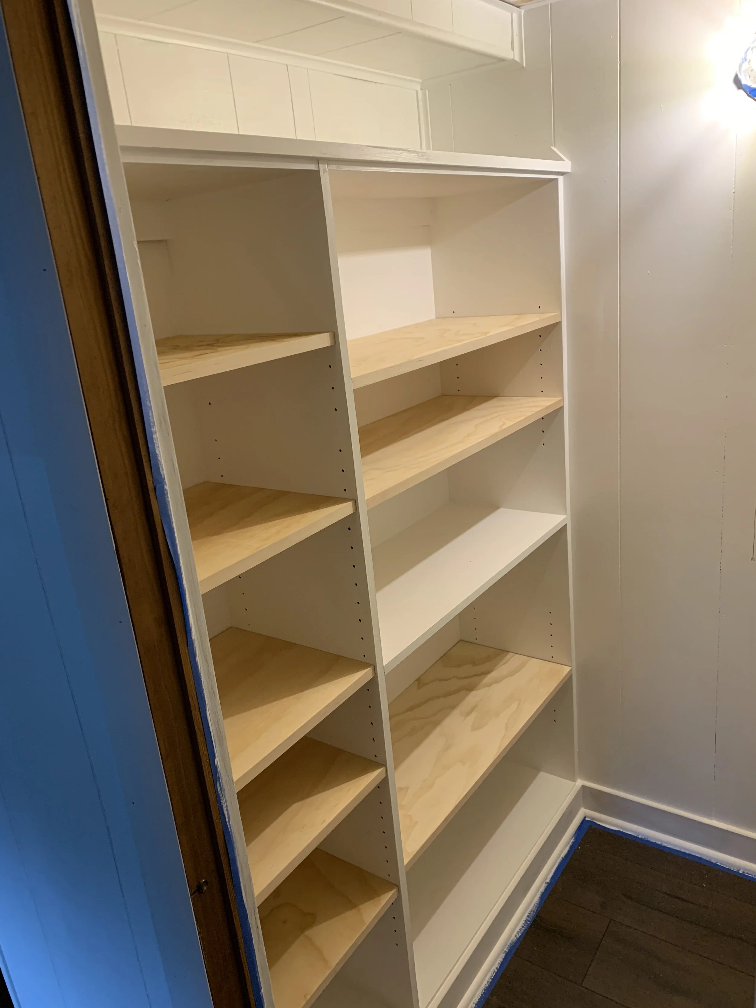 Empty white wooden bookshelf with five shelves in a room with white walls and dark wood floor.