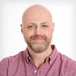 Headshot of a smiling man with a bald head and beard, wearing a burgundy button-up shirt, against a white background. Trusted handyman.