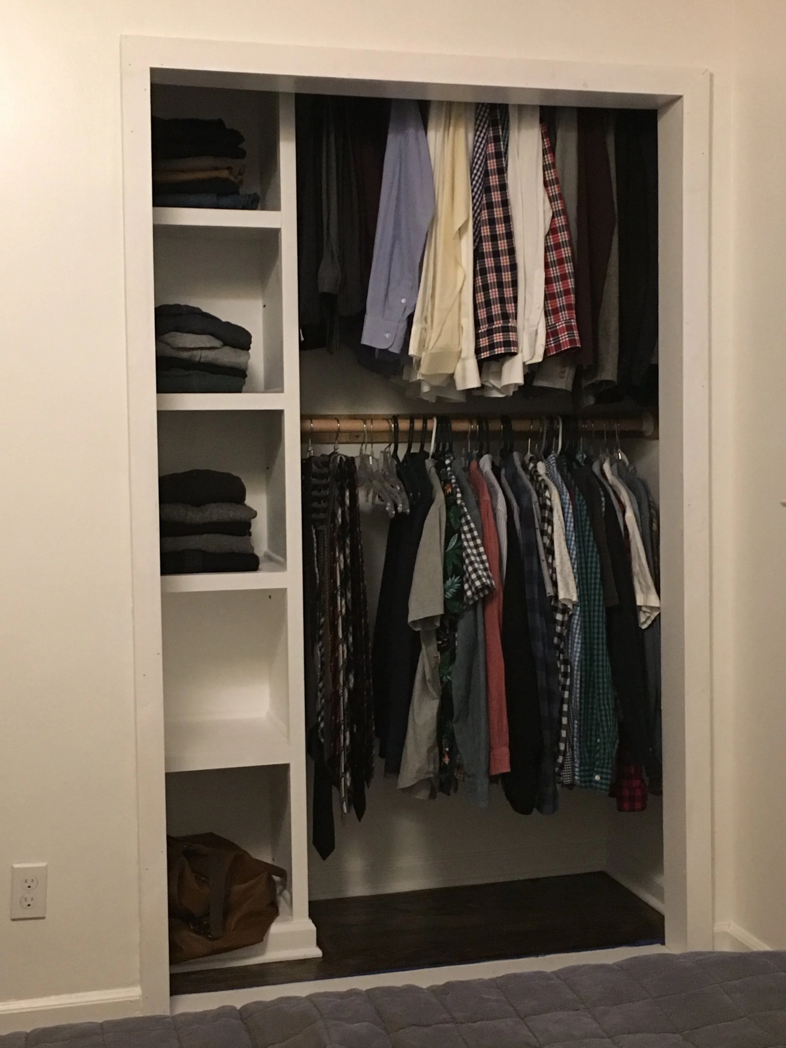 Open closet with folded clothes on shelves and shirts on hanging rod.