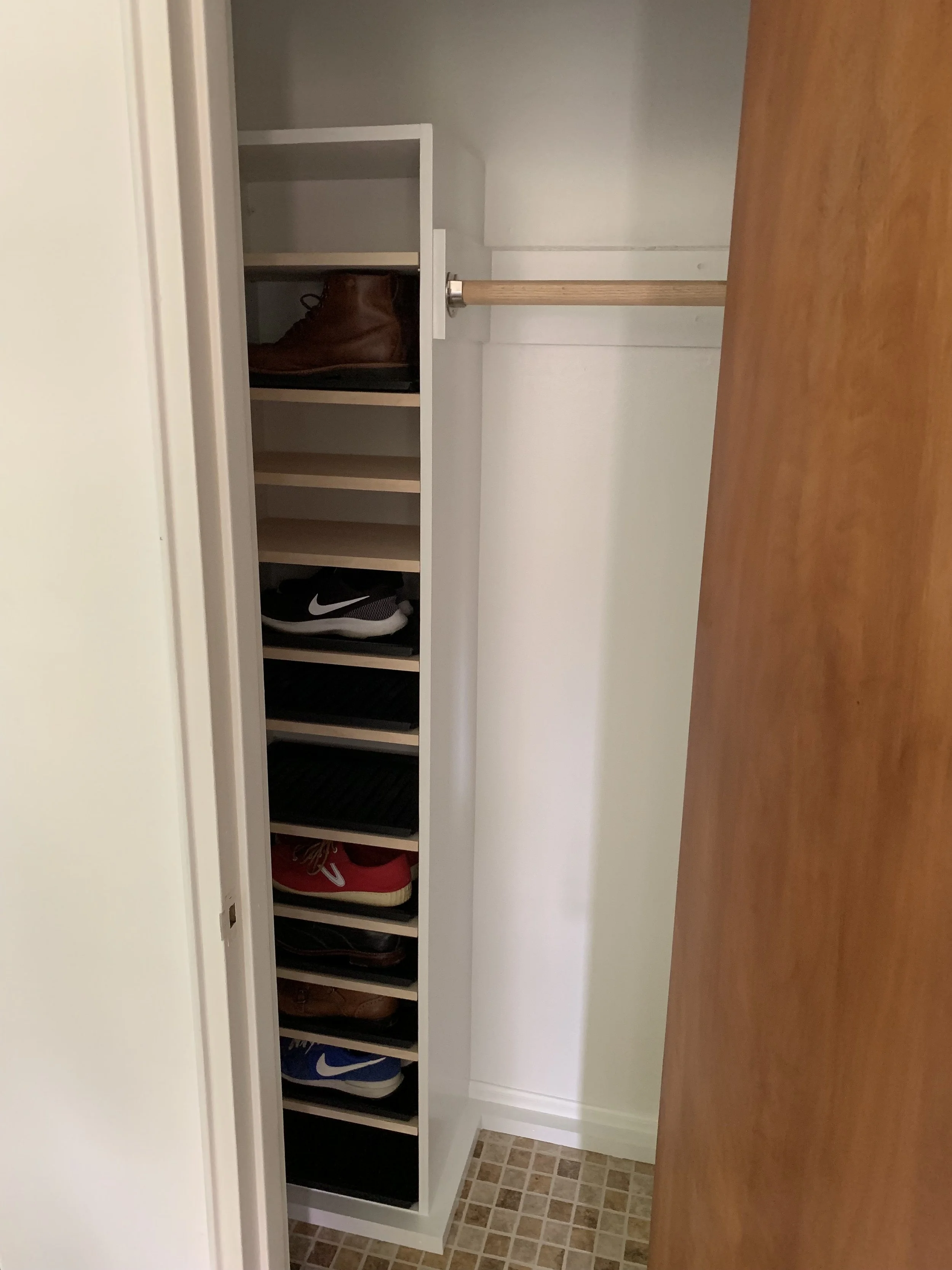 A small closet with shelves containing shoes, and an empty hanging rod for clothes.