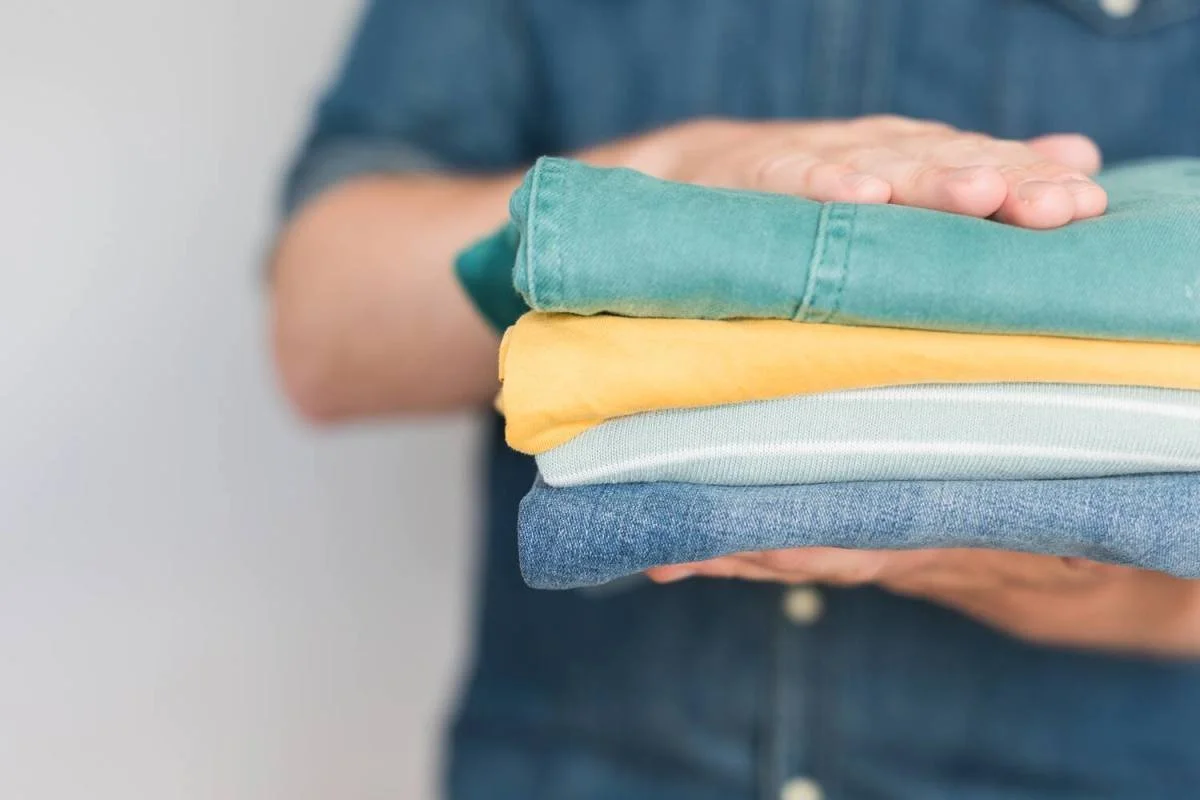 Person holding folded clothes in various colors, including blue, white, yellow, and teal.