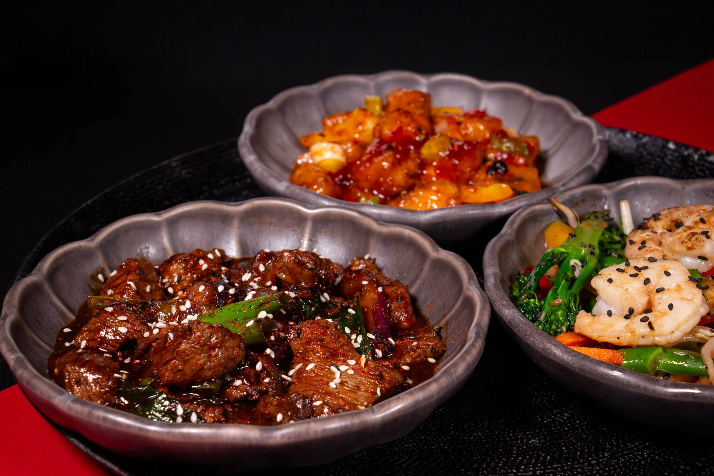 Drie kommen met verschillende Aziatische gerechten, waaronder een met rundvlees in saus, een met garnalen en groenten, en een met kip en groenten.