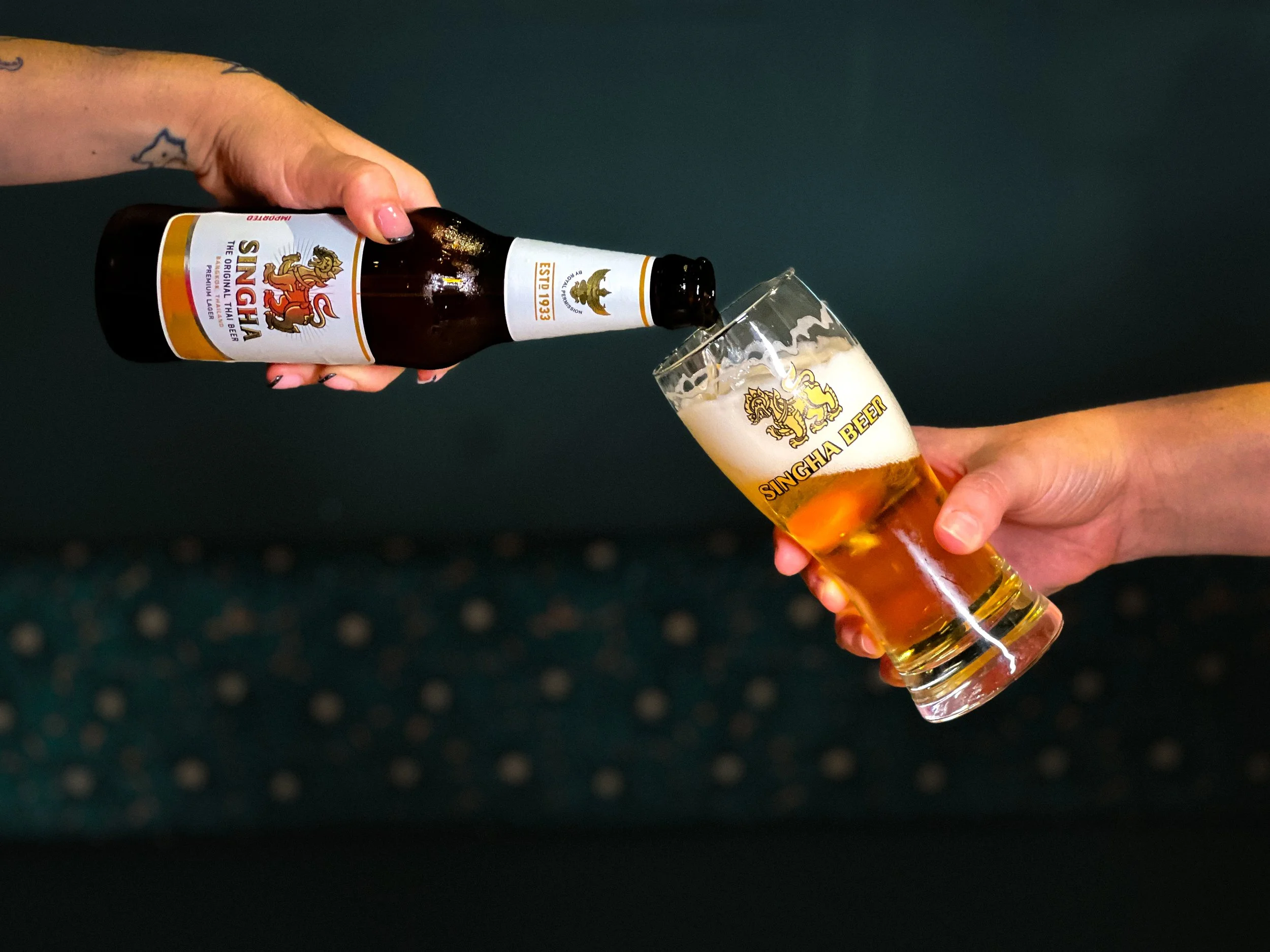 Person die een fles Singha bier schenkt in een glas met Singha Beer logo