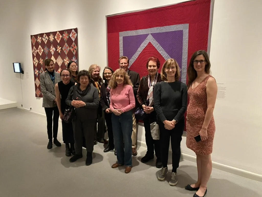 A group poses for a picture in front of a massive red quilt hung on a wall