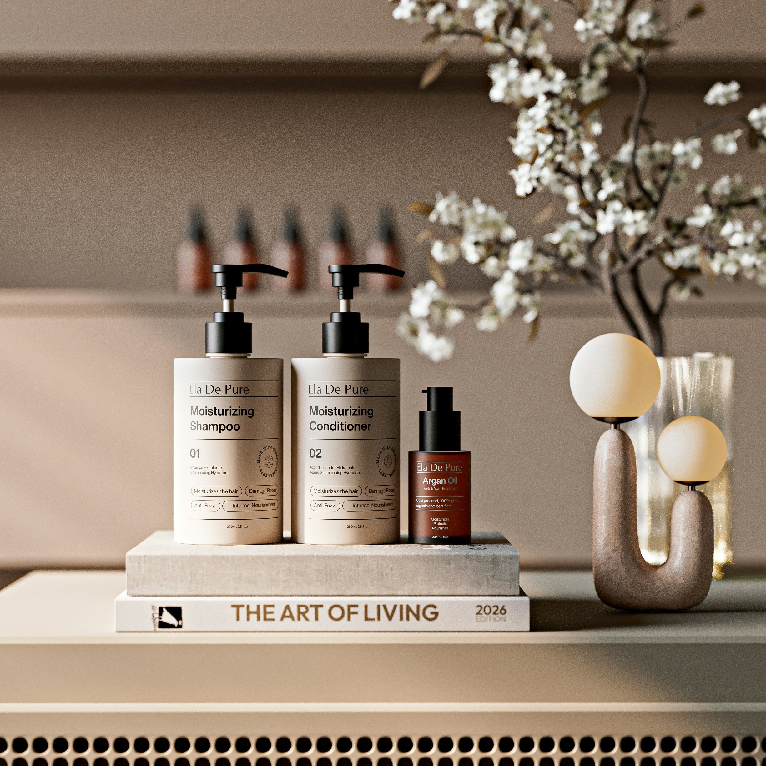 Decorative shelf with beauty products, a flower arrangement, and a large candle holder. Items include two bottles of Ela De Pure moisturizing shampoo and conditioner, a small bottle of Argan Oil, a stack of books titled 'The Art of Living' and another gray book, with a background of a beige wall and some bottles.