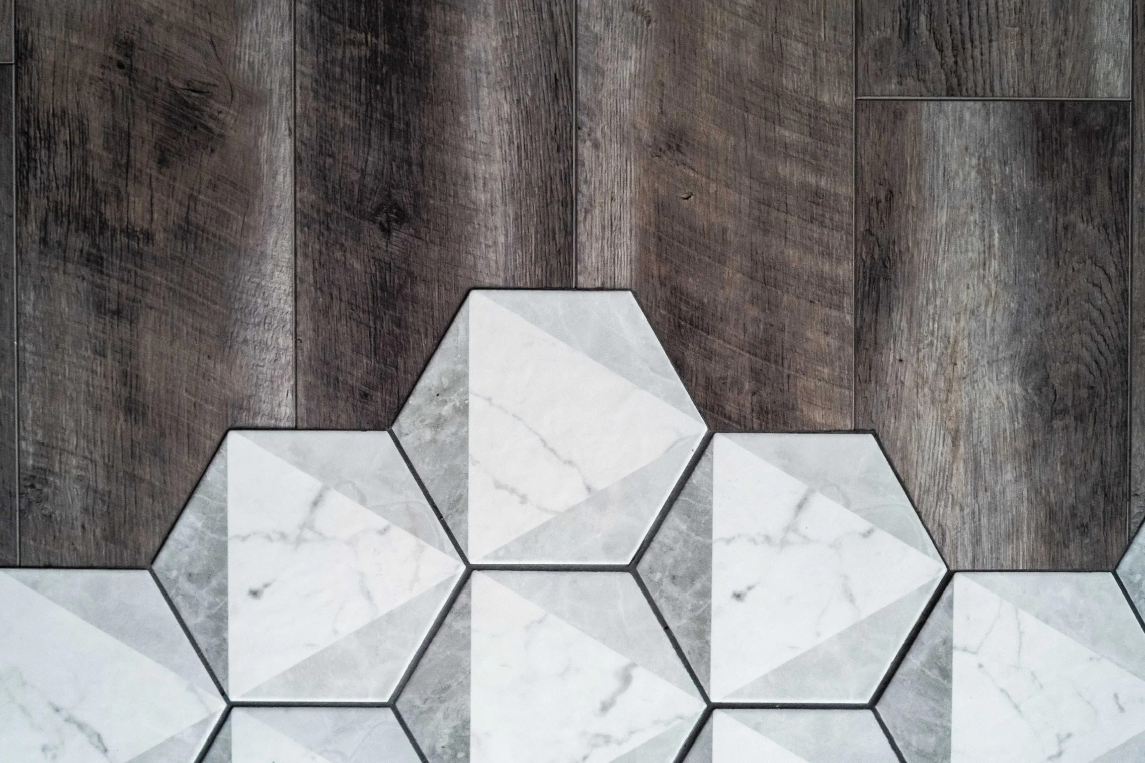 Close-up of different brown and gray tiles, including wood-look planks and geometric marble tiles on a floor.